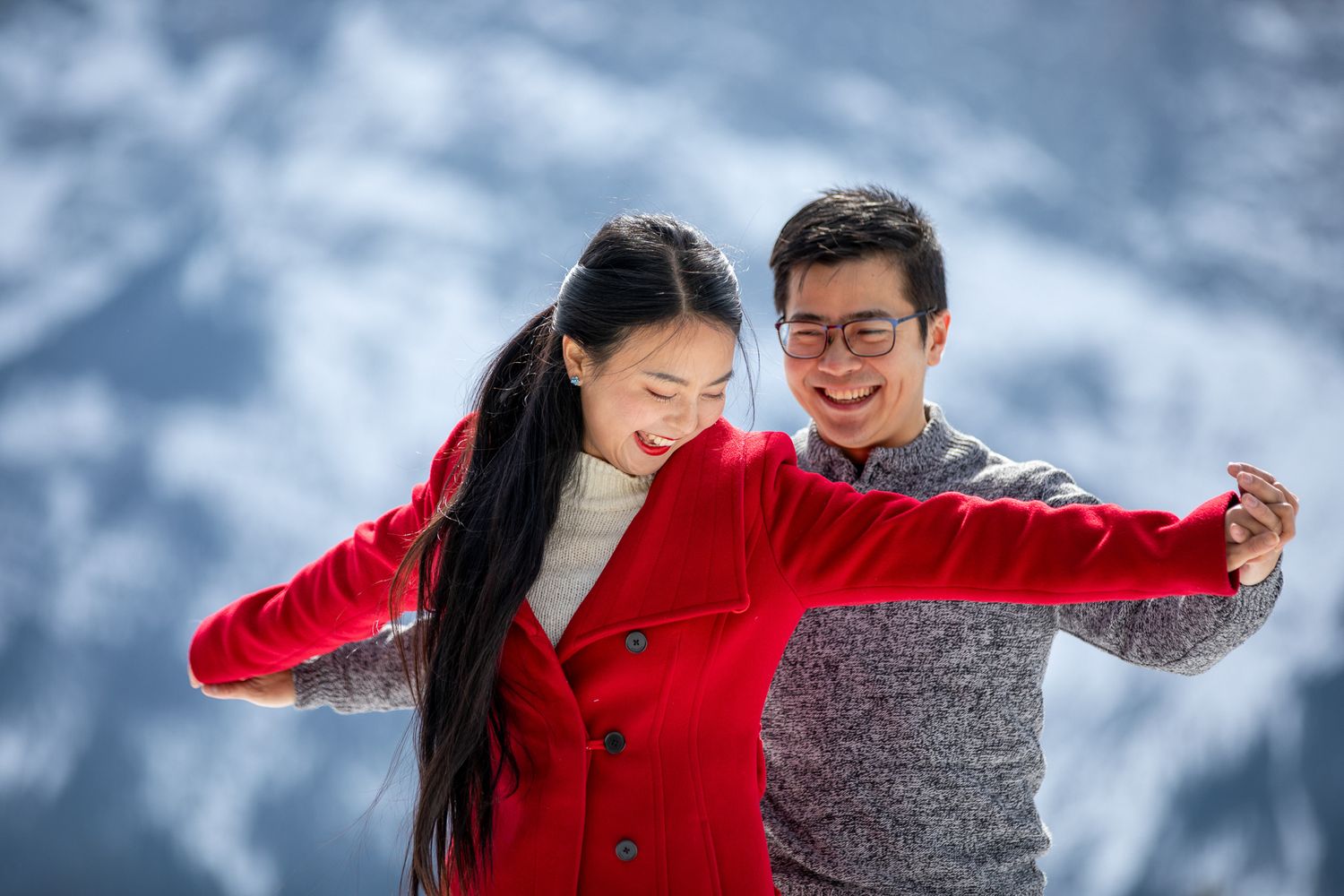 A couple in red and grey winter outfits dance together in a snowy outdoor setting  in Banff, AB.