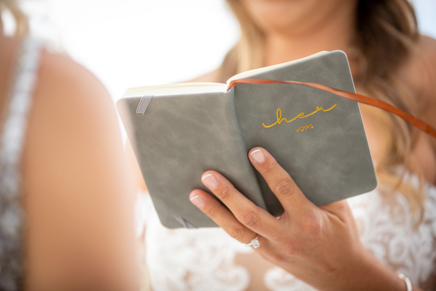 Bride in white lace dress reading handwritten wedding vows from a grey suede journal with gold script lettering at Kicking Horse Resort, BC