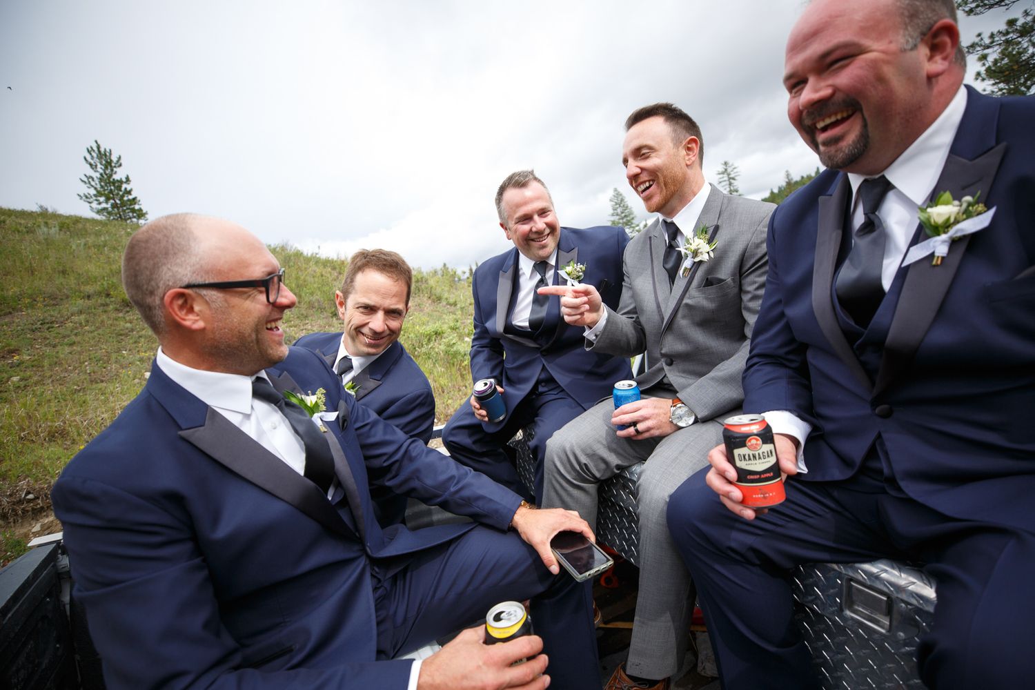 Groomsmen in navy suits laughing and celebrating together outdoors on a wedding day at Cherry creek estate