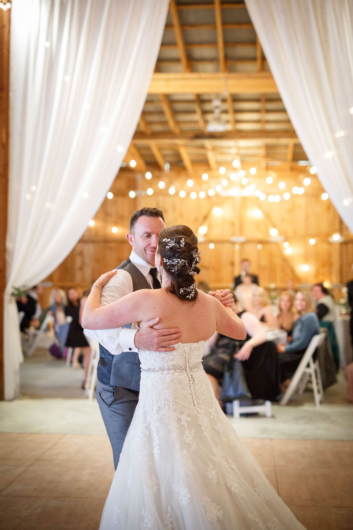 Bride and groom share their first dance in a rustic barn wedding venue adorned with string lights and white draping Cherry creek estate
