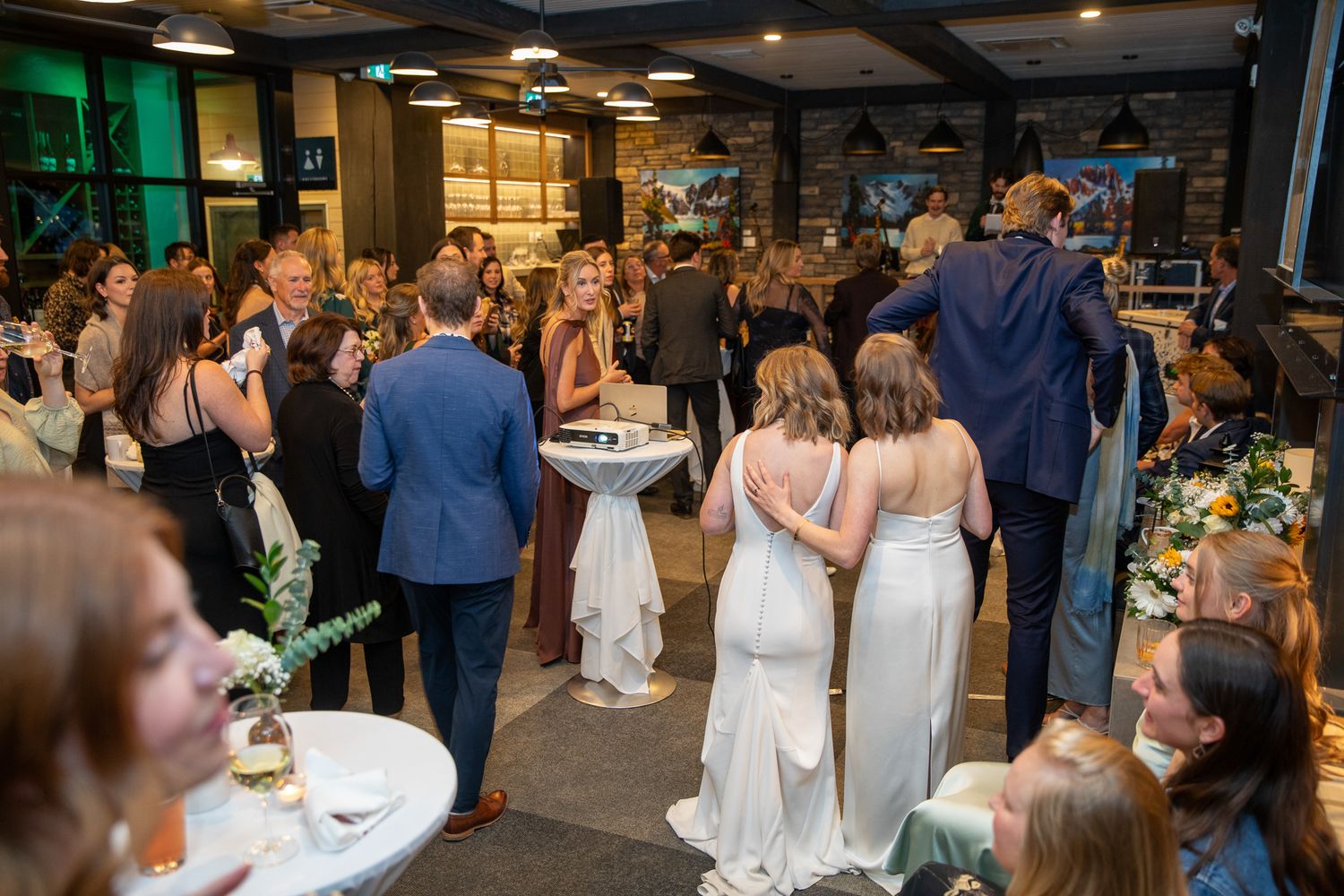 Wedding reception guests mingle and dine in an elegant indoor venue with warm lighting and modern decor.