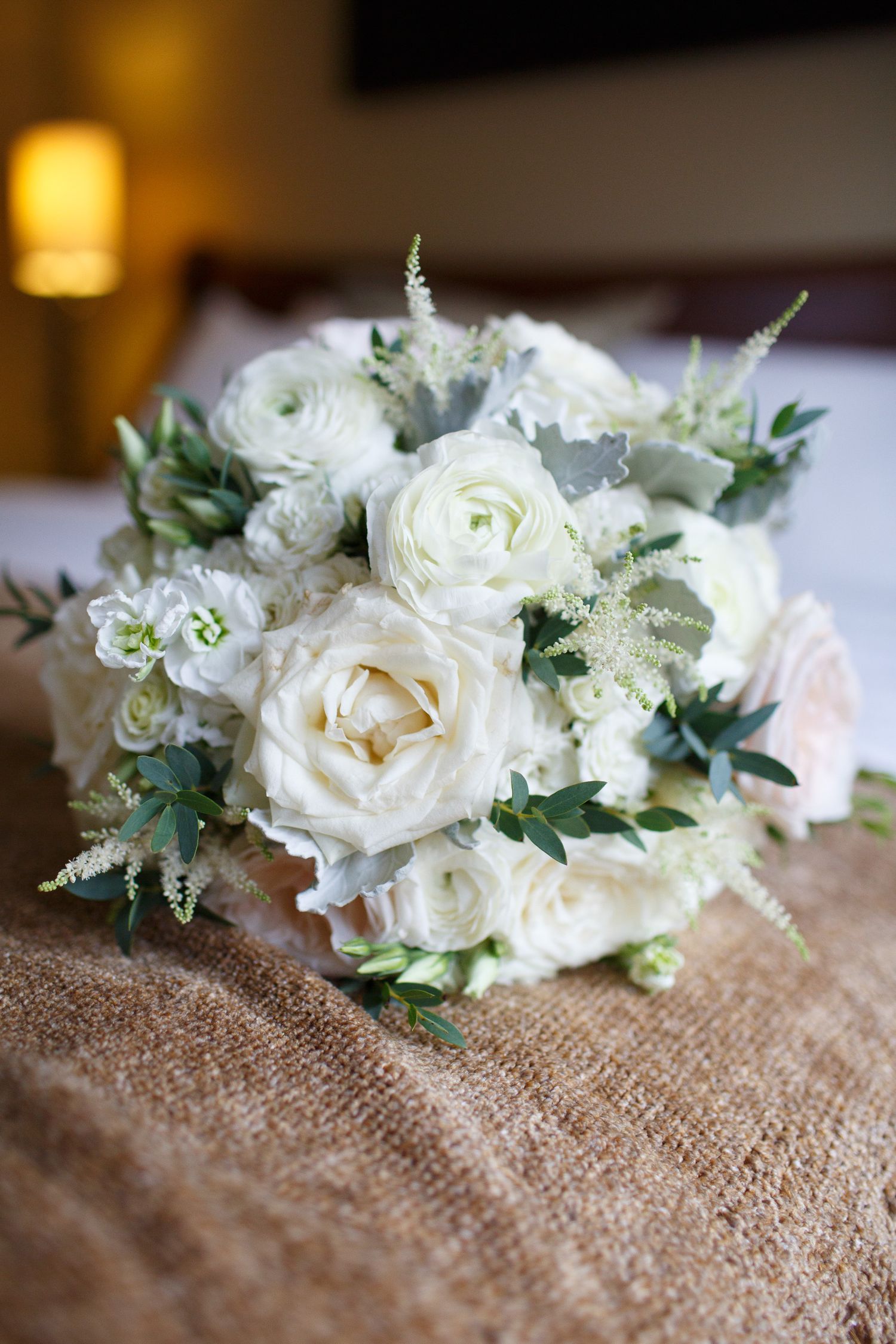 White roses and delicate floral arrangements rest on rustic burlap fabric in a romantic wedding setting.