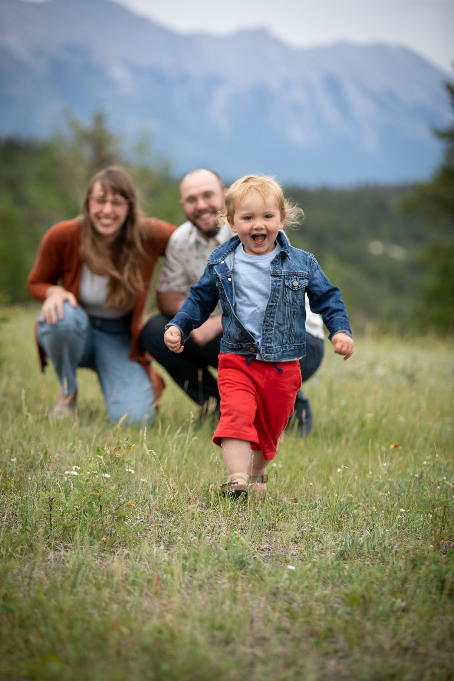 Family plays together running through a mountain meadow on a summer afternoon in Banff, AB.