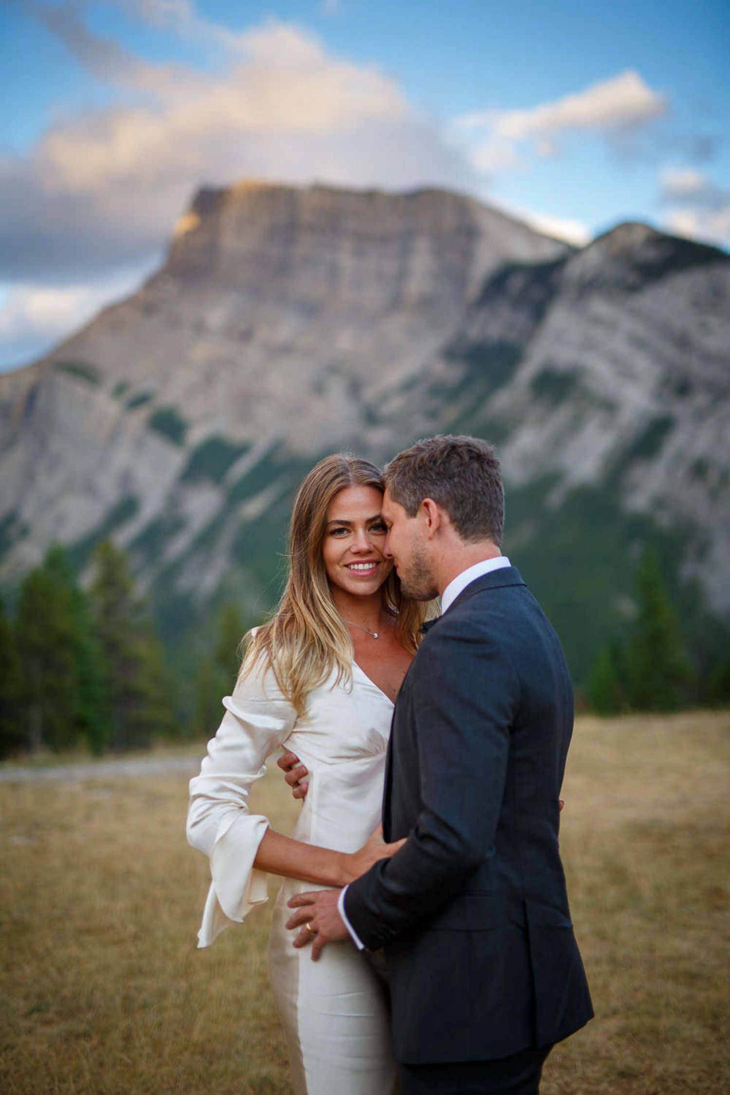 A couple shares romantic moments in front of majestic mountain peaks of Mount Rundle during an outdoor photo session in Banff.