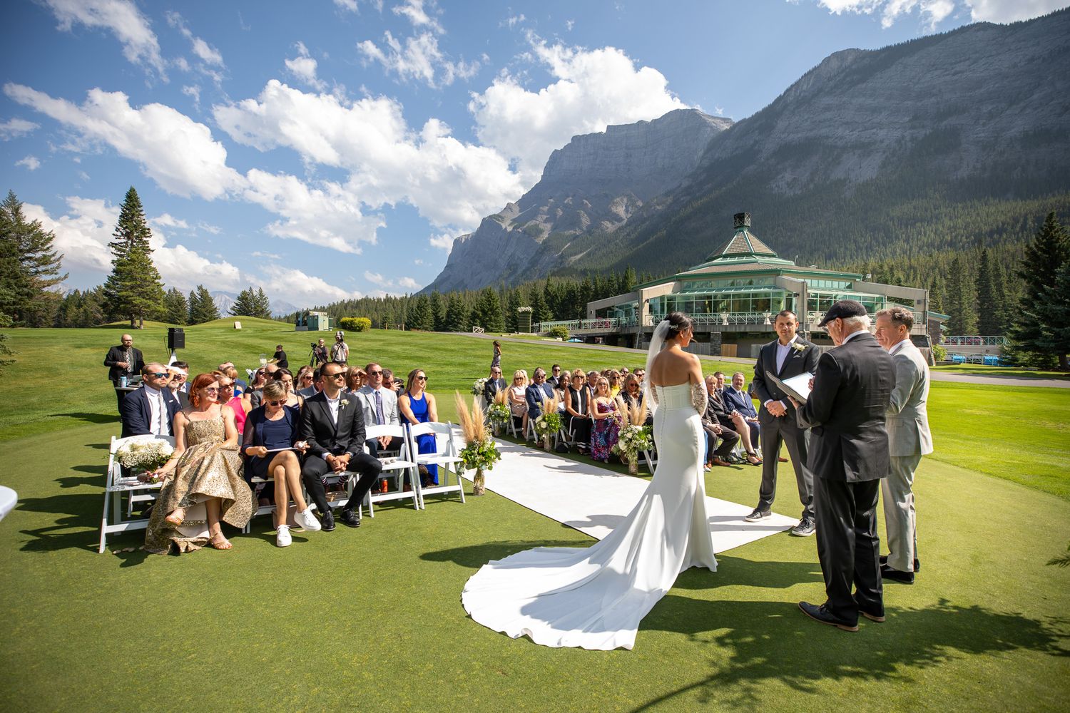 Outdoors wedding ceremony at the Fairmont Banff Springs golf course venue in Banff, Alberta. Beautiful mountain peaks in the backgrounds.