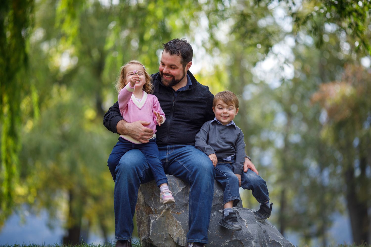 A family sits together on a park bench surrounded by lush green trees on a sunny autumn day Timber Ridge in Windermere, BC