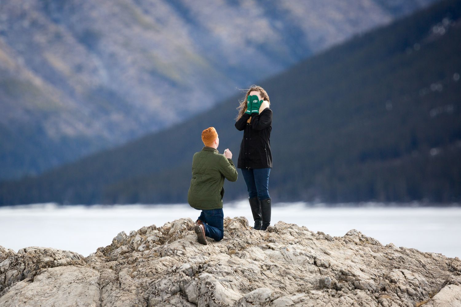 Couple captured during a surprise proposal on a rock at Minnewanka Lake in Banff National Park