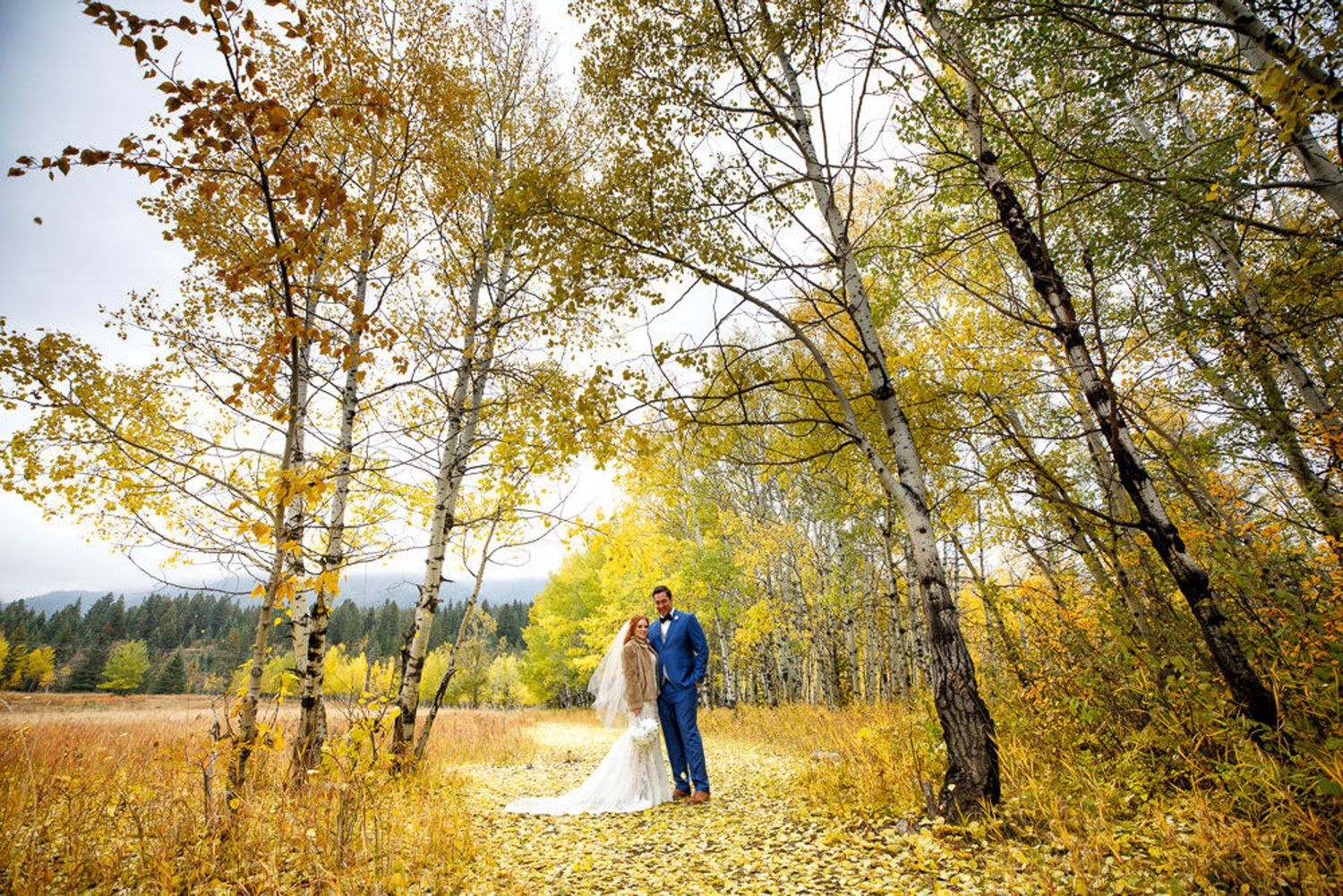 Couple stands together among golden autumn trees during a fall wedding photoshoot in a scenic forest setting. Canmore Alberta.