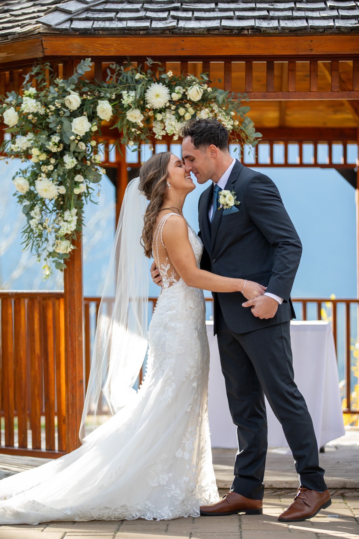 A romantic wedding couple shares tender moments under a rustic wooden gazebo decorated with white floral arrangements at Silvertip resort.