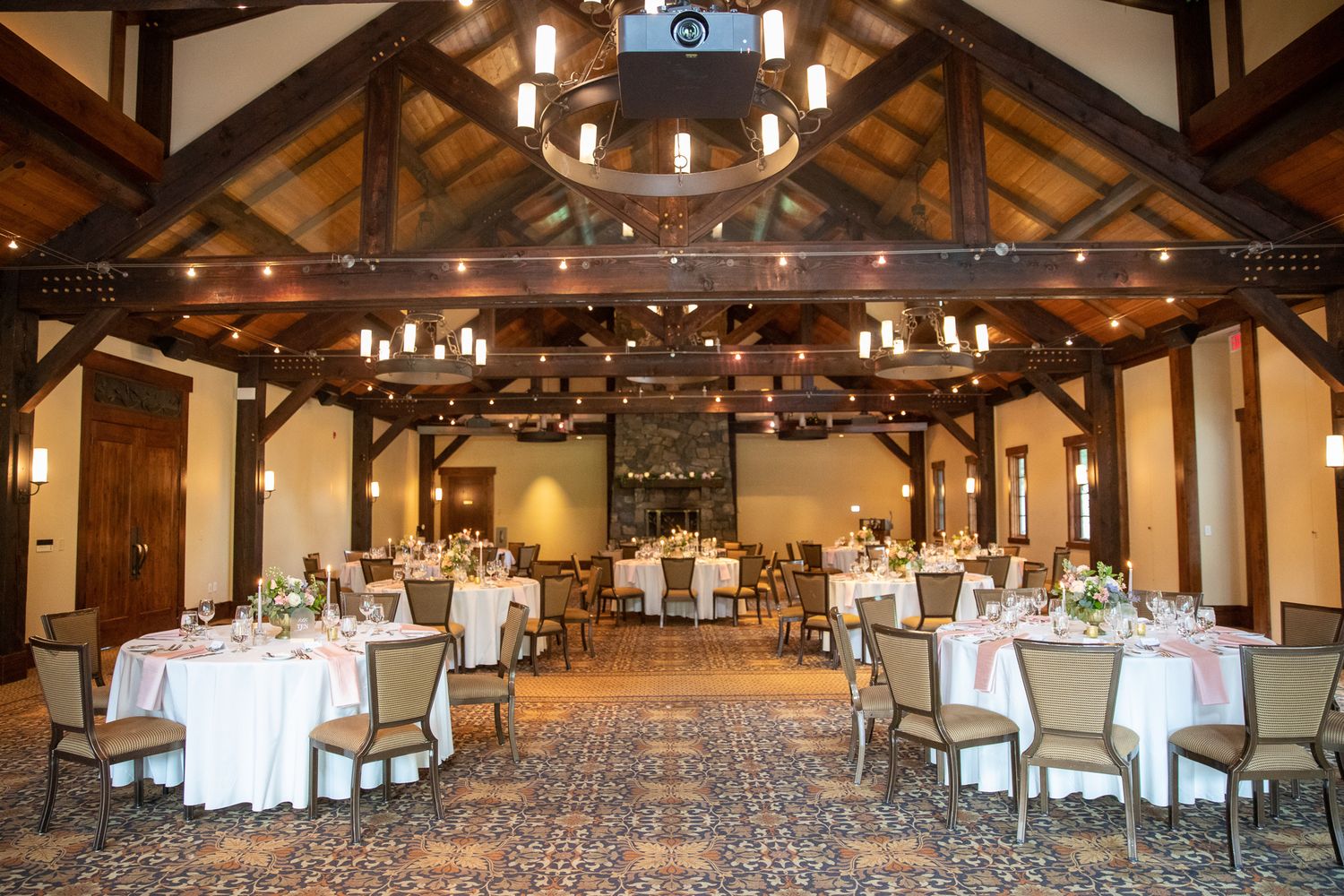 Elegant Silvertip resort banquet hall with rustic wood beams, chandelier lighting, and round tables set for a wedding reception In Canmore