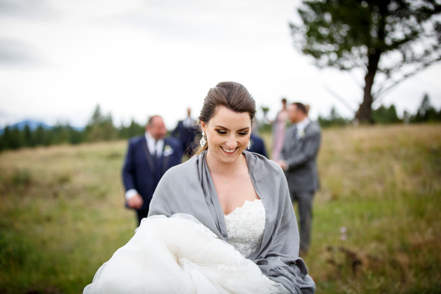 Smiling bride in white gown and gray shawl walks through a green meadow on her wedding day Cherry creek estate