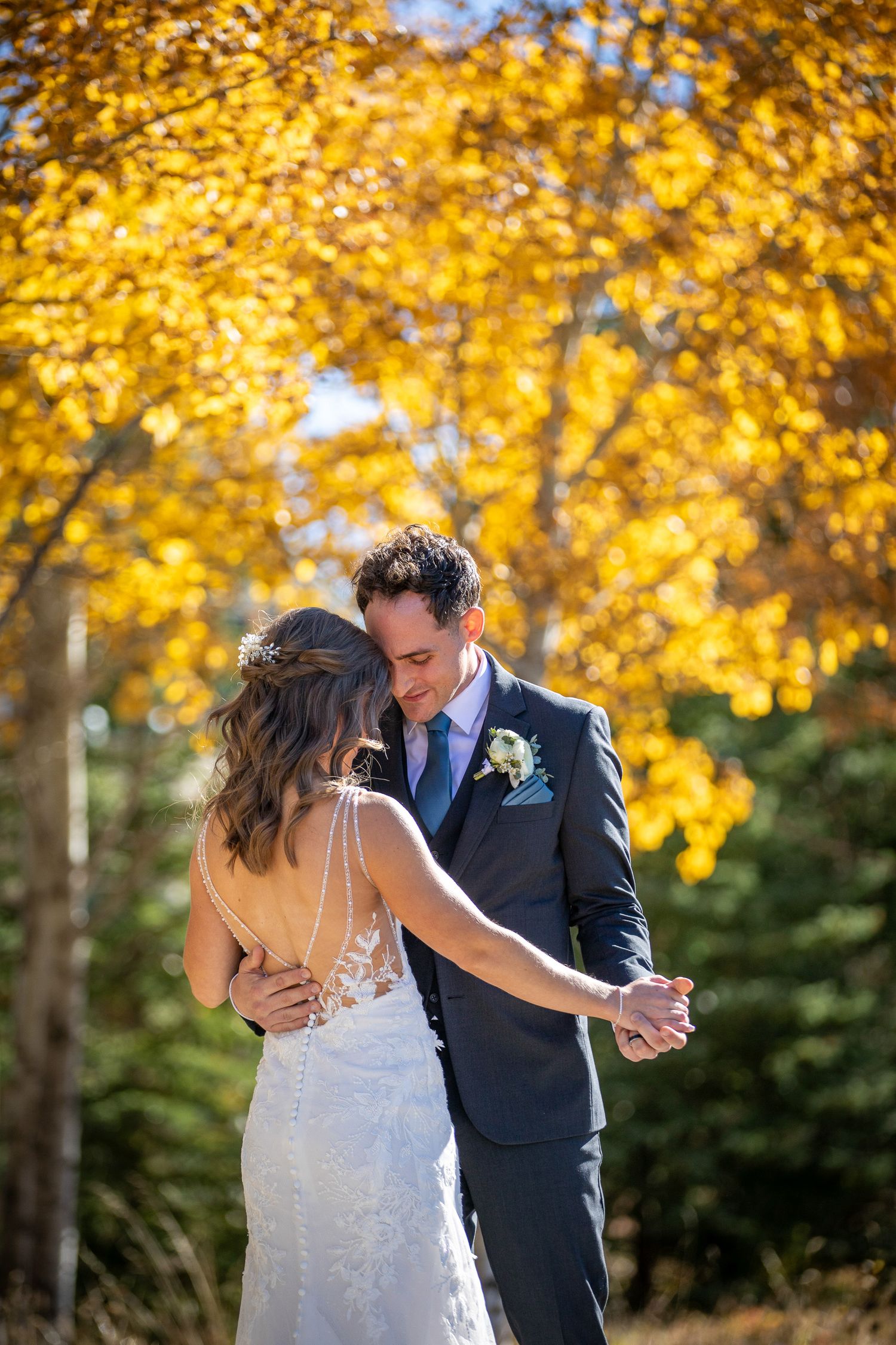 A couple shares a romantic moment under vibrant yellow autumn foliage during their wedding day celebration in Canmore Benchland Trails