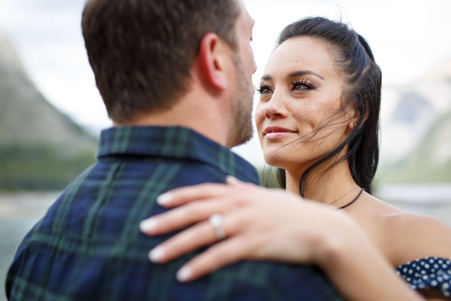 A romantic couple embraces and smiles at each other while standing outdoors at Lake Minnewanka in Banff.
