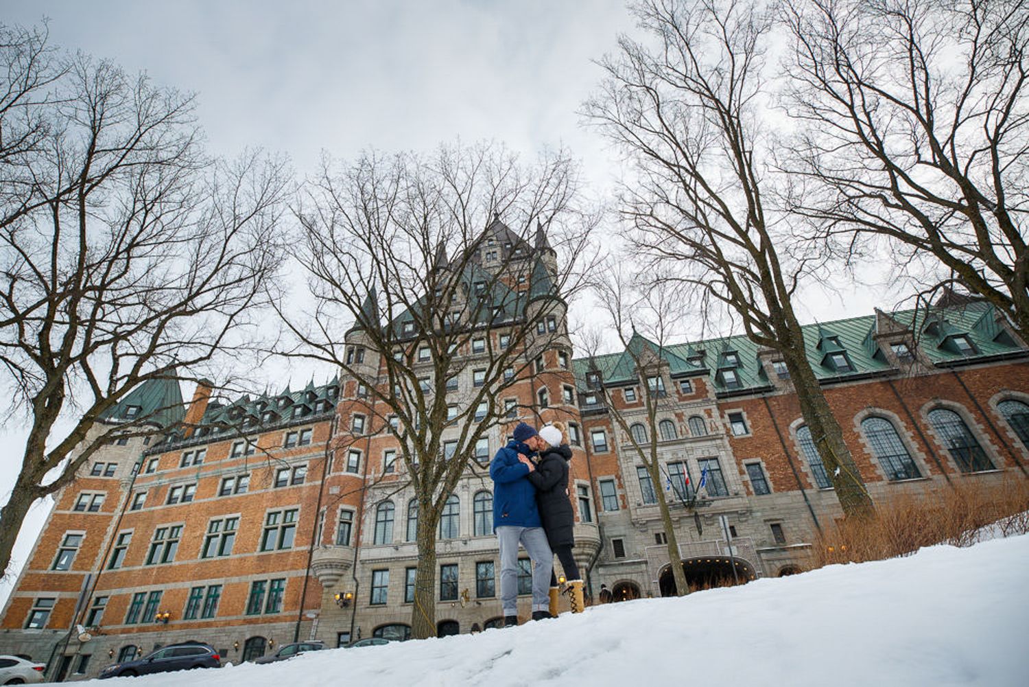 A couple embraces in front of the historic Chateau Frontenac hotel in Quebec City during winter in a charming town of Old Quebec City.