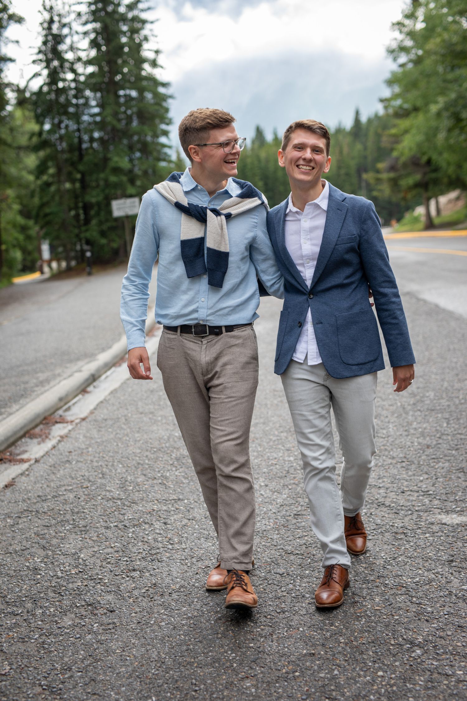 A LGBTQ couple walking together on a gravel path surrounded by evergreen trees at lake Minnewanka in Banff National Park.