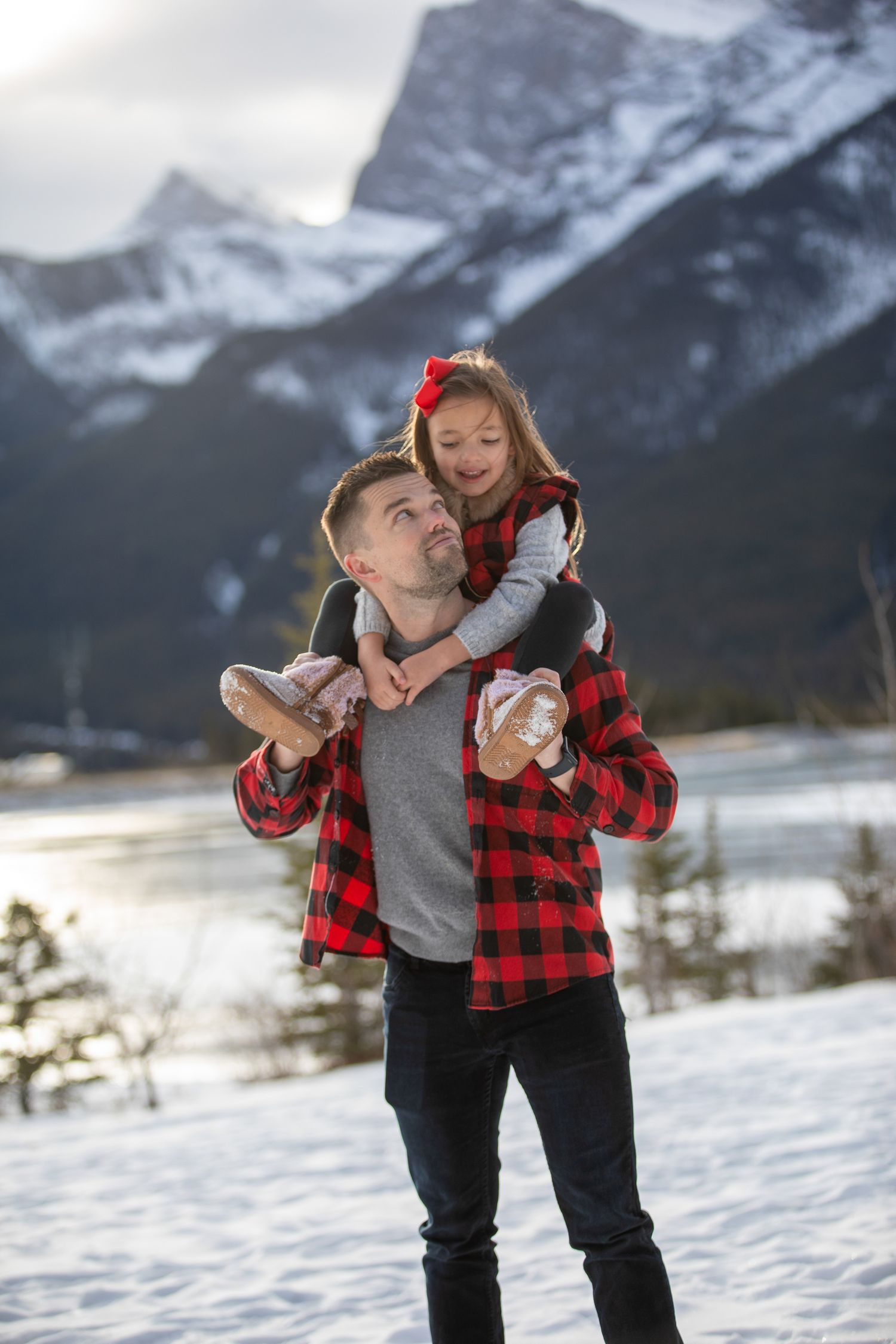 A parent and child share a playful moment in the snow with mountains of Banff National Park as their backdrop.