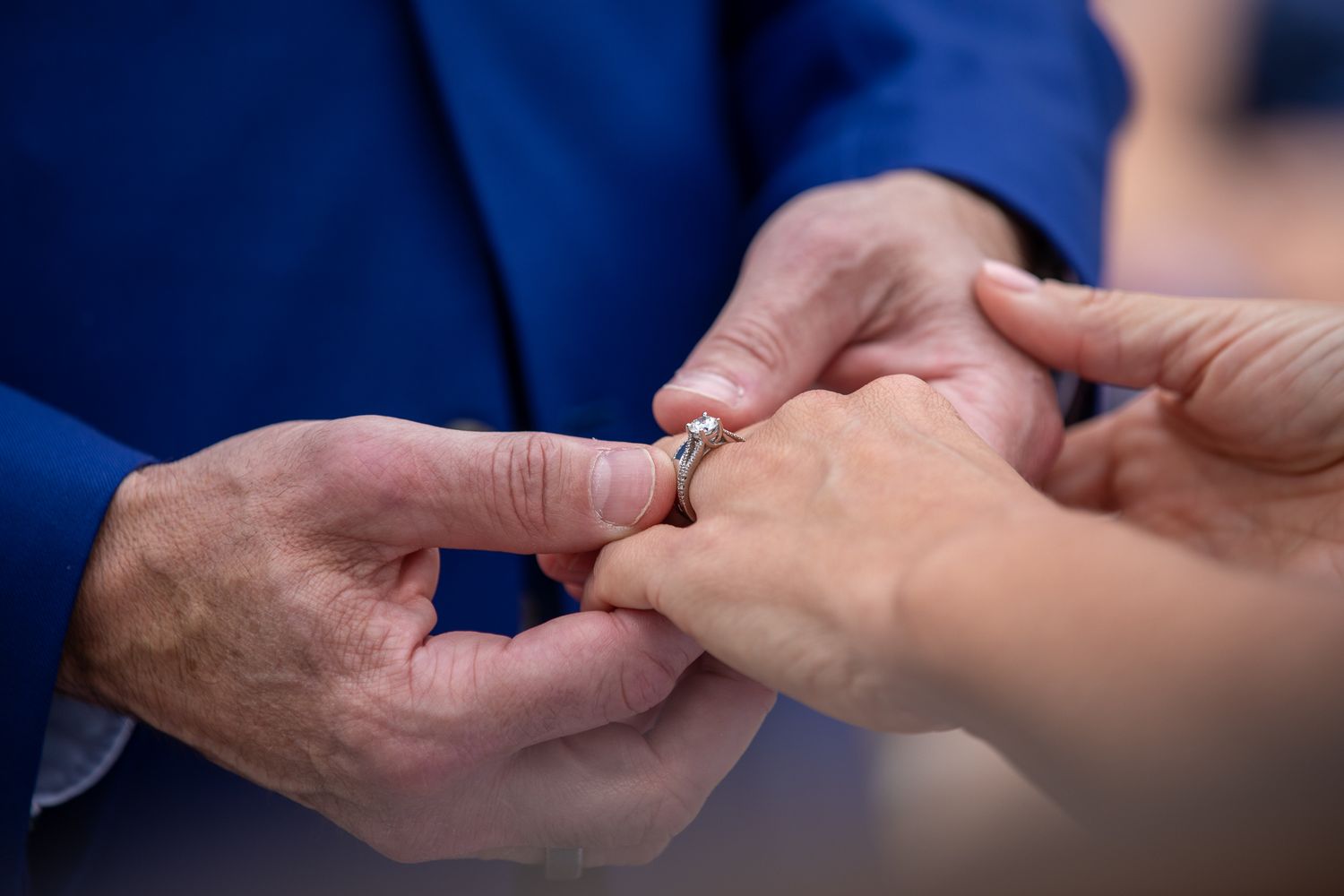 Close-up of a groom placing a diamond engagement ring on his bride's finger during a wedding ceremony.