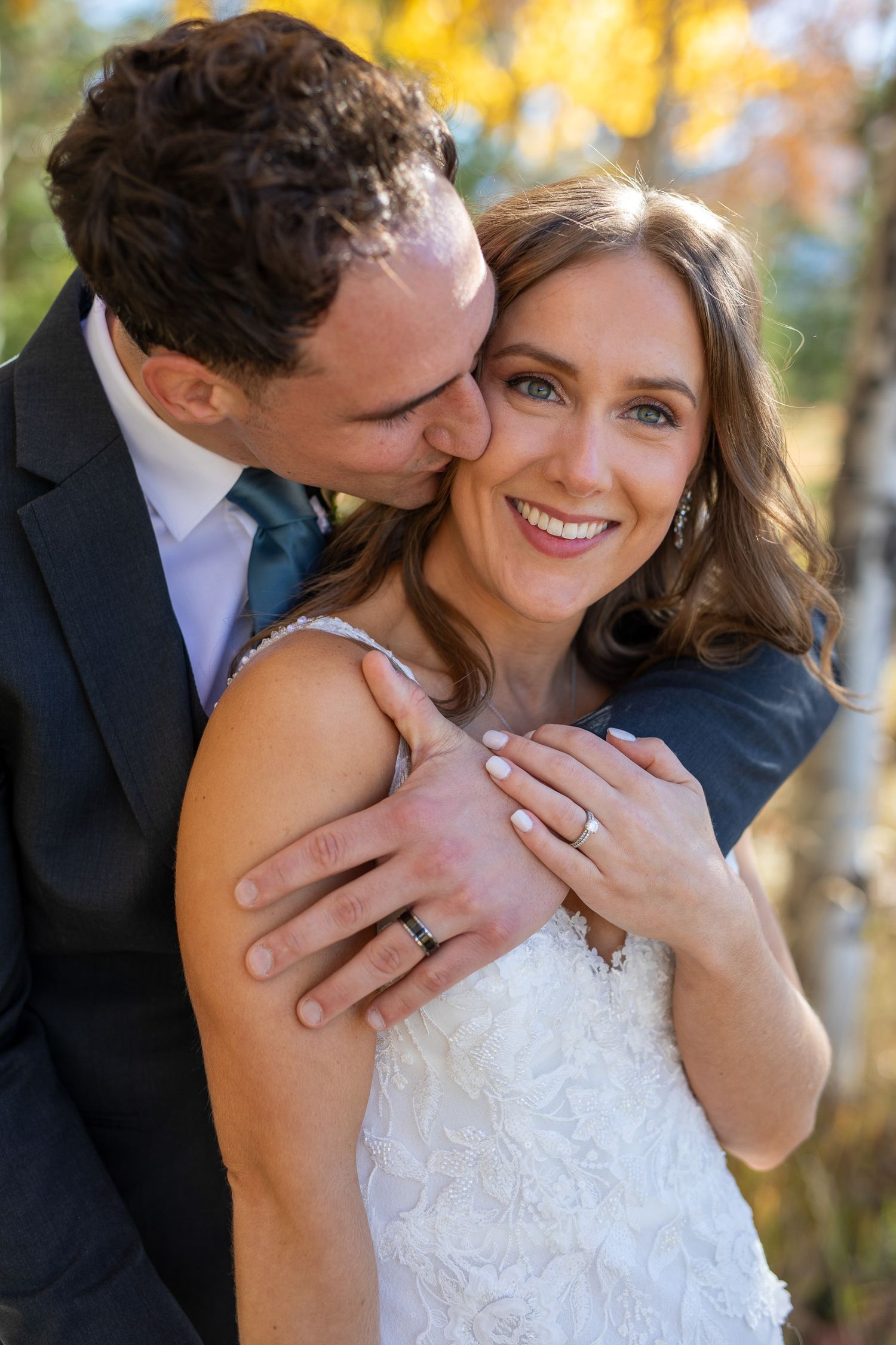A romantic wedding portrait outdoors with autumn colors in the background, featuring a white lace dress and dark suit at Quarry lake Canmore