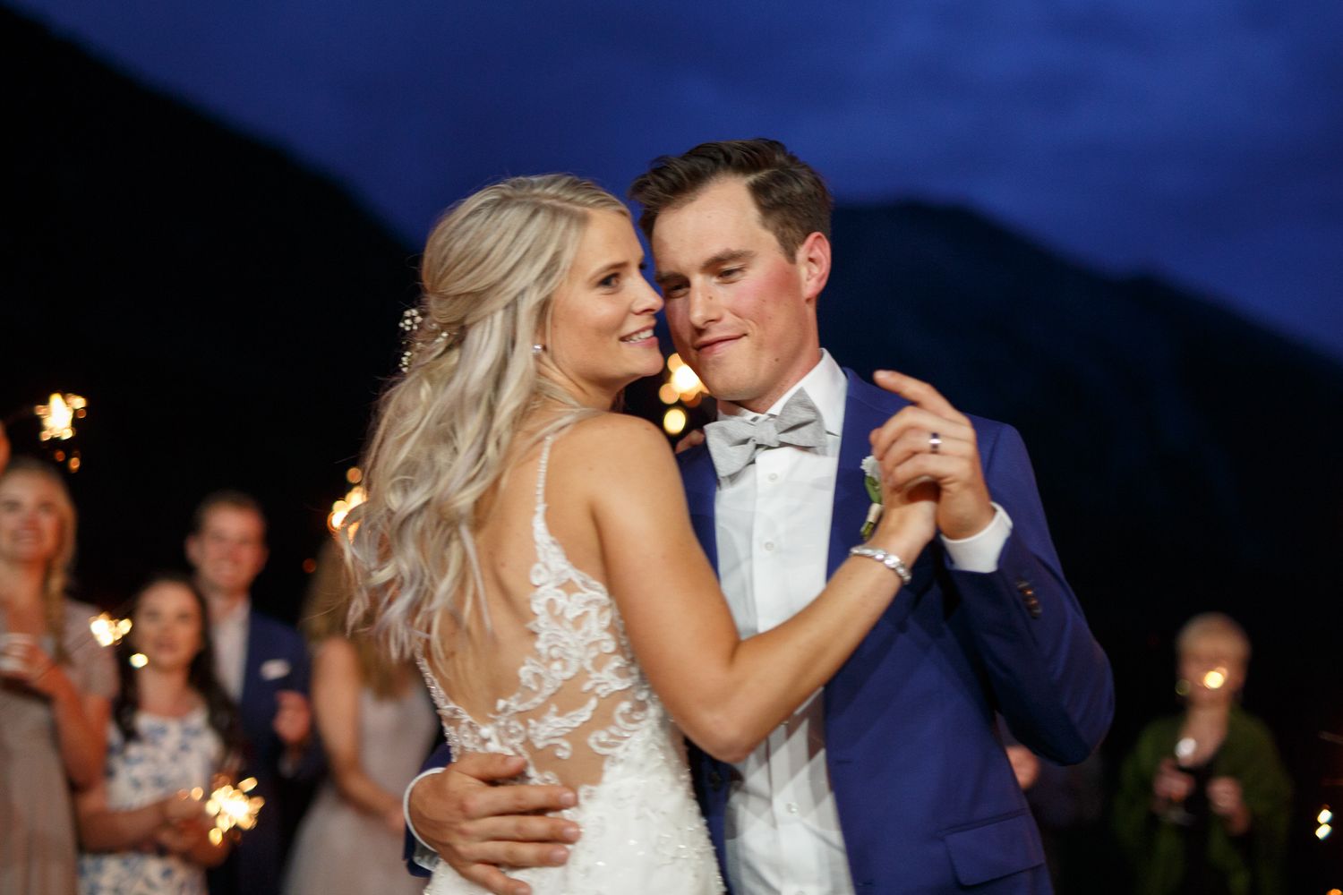 Romantic wedding couple dances together during evening celebration with sparklers glowing in the background. Silvertip resort in Canmore.