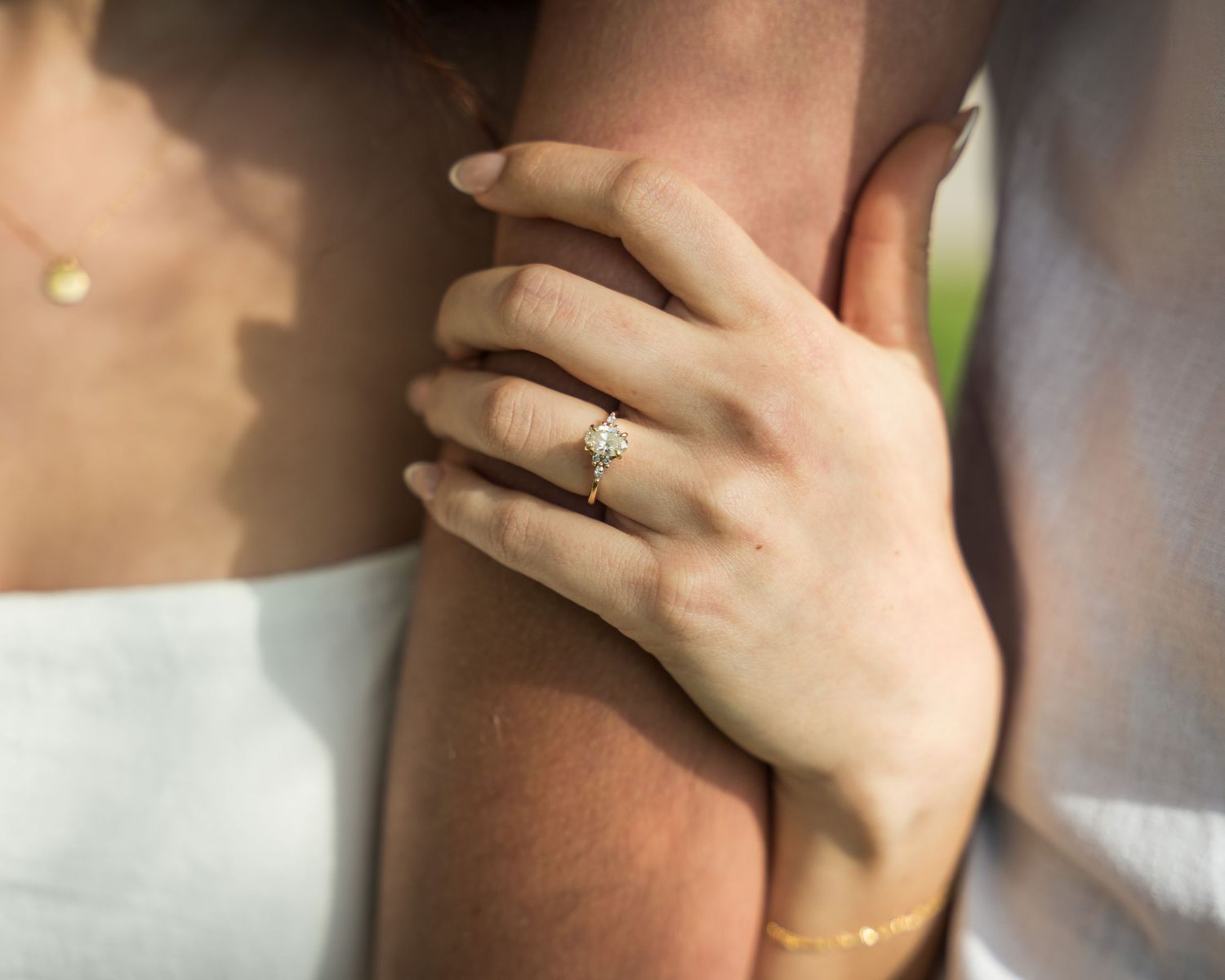 Close-up of a woman's hand with a diamond engagement ring resting on a man's arm.