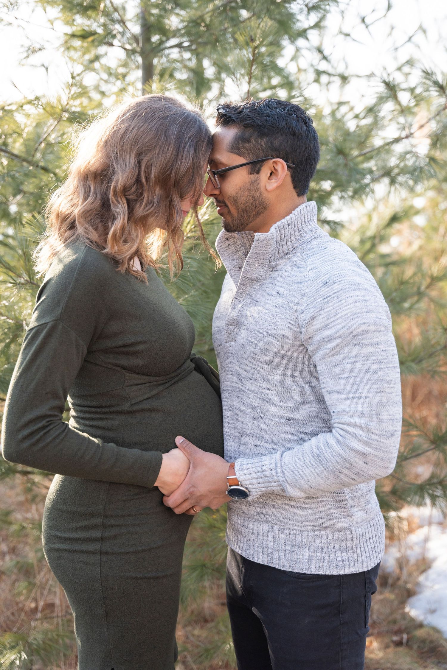 Intimate moment between couple during maternity photoshoot in snowy outdoor setting.