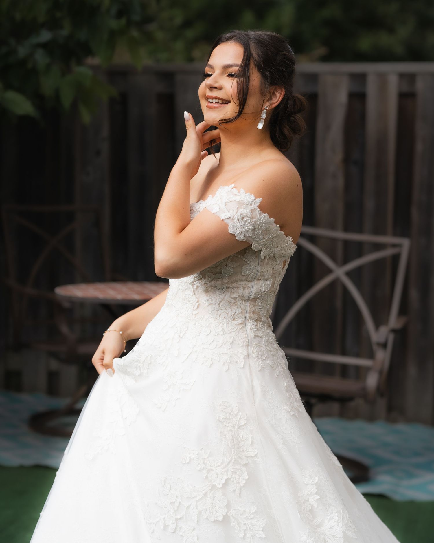 A bride in a lace wedding gown poses elegantly in a garden setting.