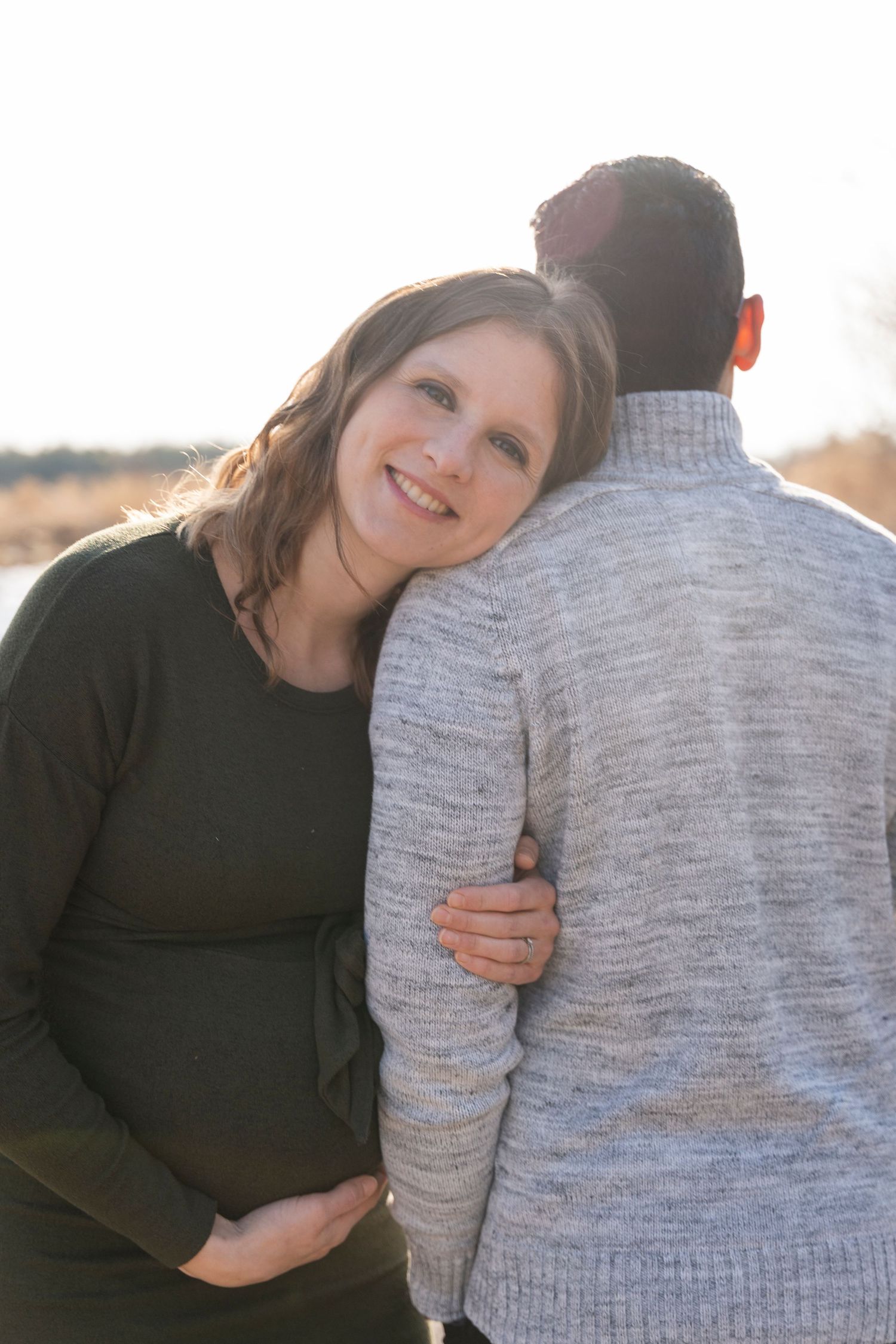 Intimate maternity portrait of couple embracing outdoors in warm winter clothing.