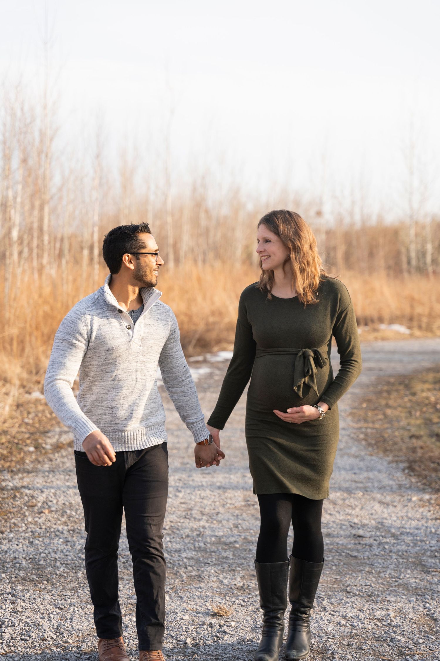 A couple takes a romantic stroll together on a gravel path surrounded by golden winter grass.