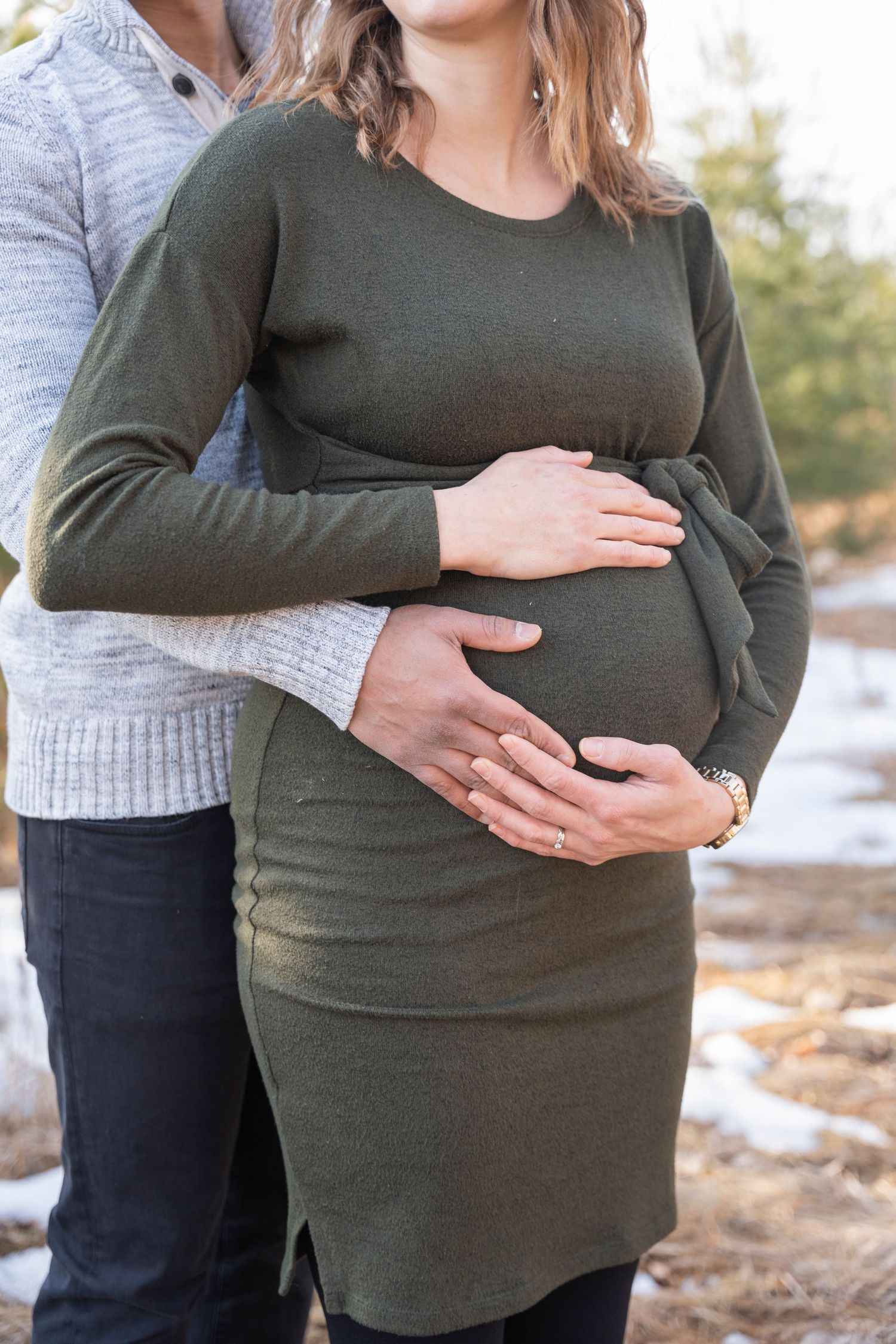 Close-up of couple's hands tenderly cradling pregnant belly in olive green dress.