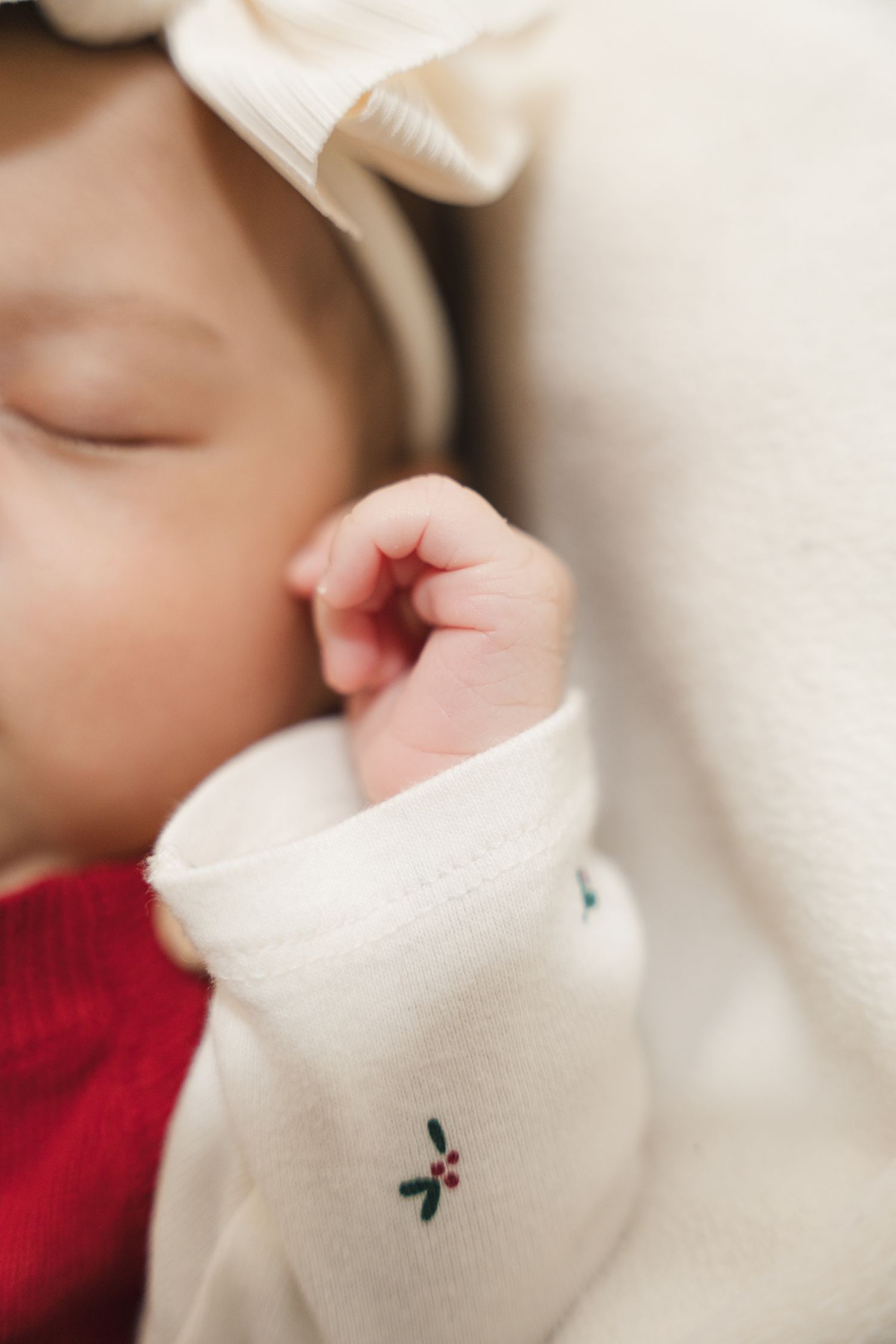 Close-up of a sleeping baby's tiny hand in a white and red outfit.