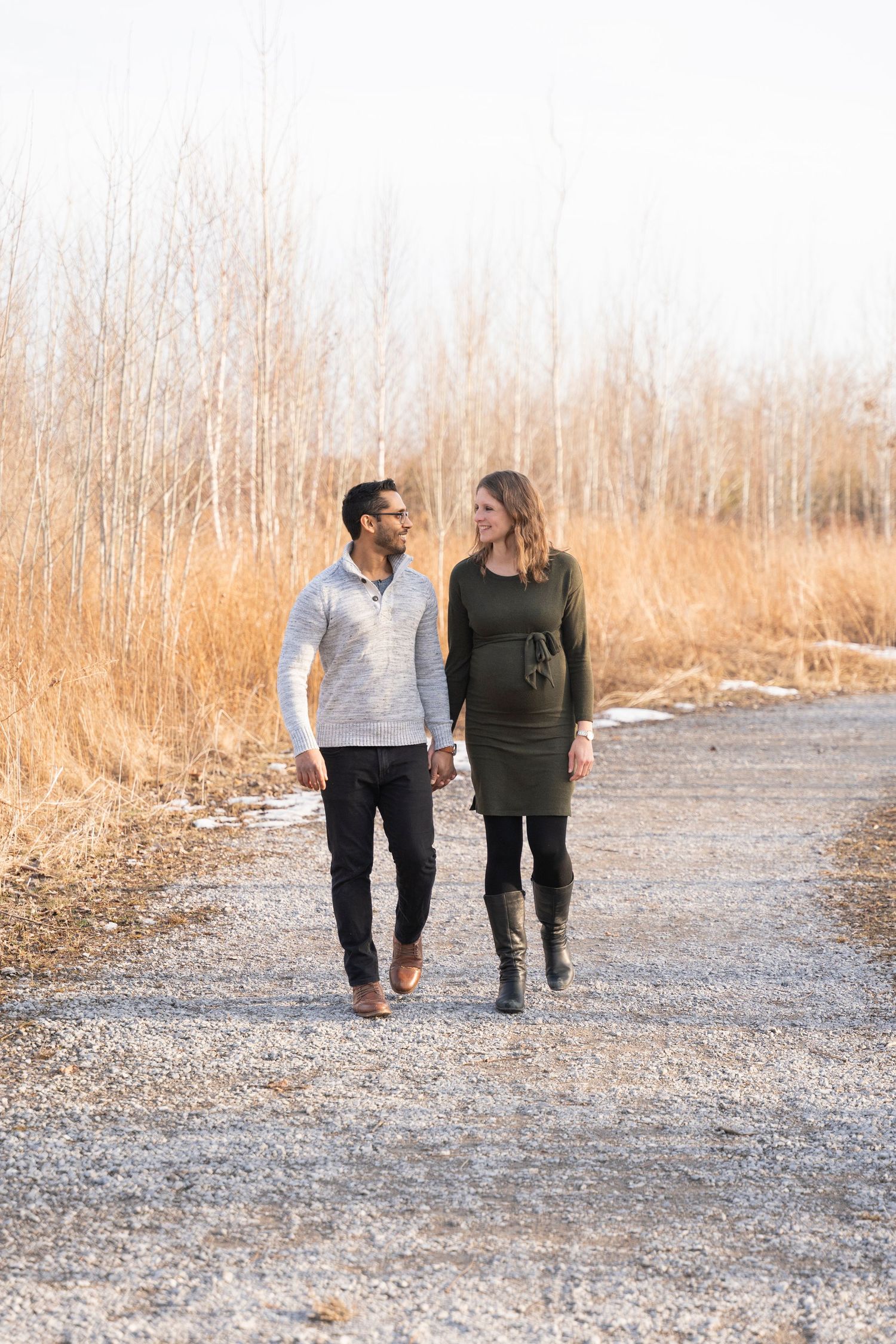 A couple walks hand in hand down a gravel path surrounded by tall golden grasses.
