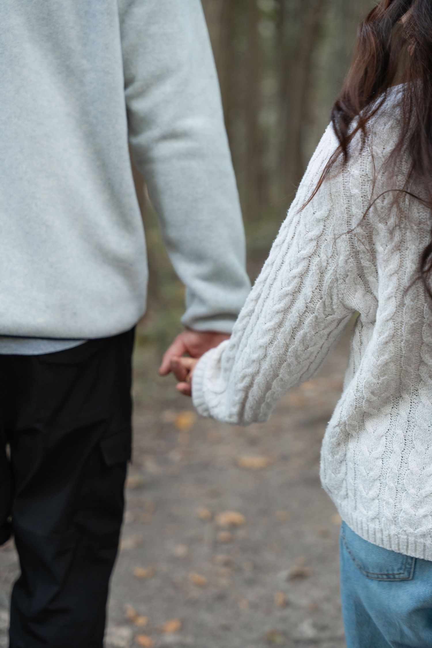 Two people holding hands while walking, wearing cozy cable knit sweaters.