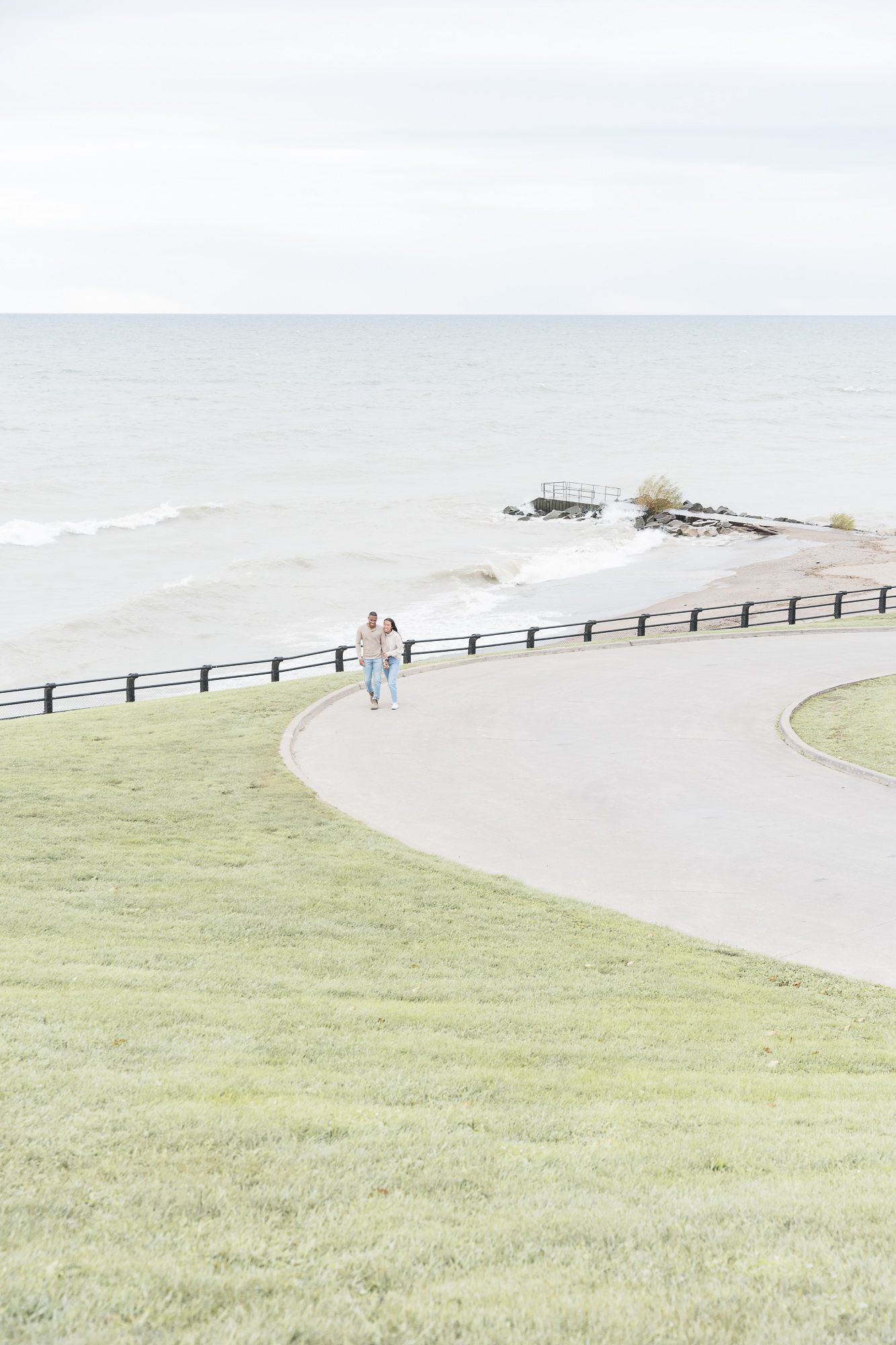 Aerial view of a coastal path with couple walking along seaside fence.