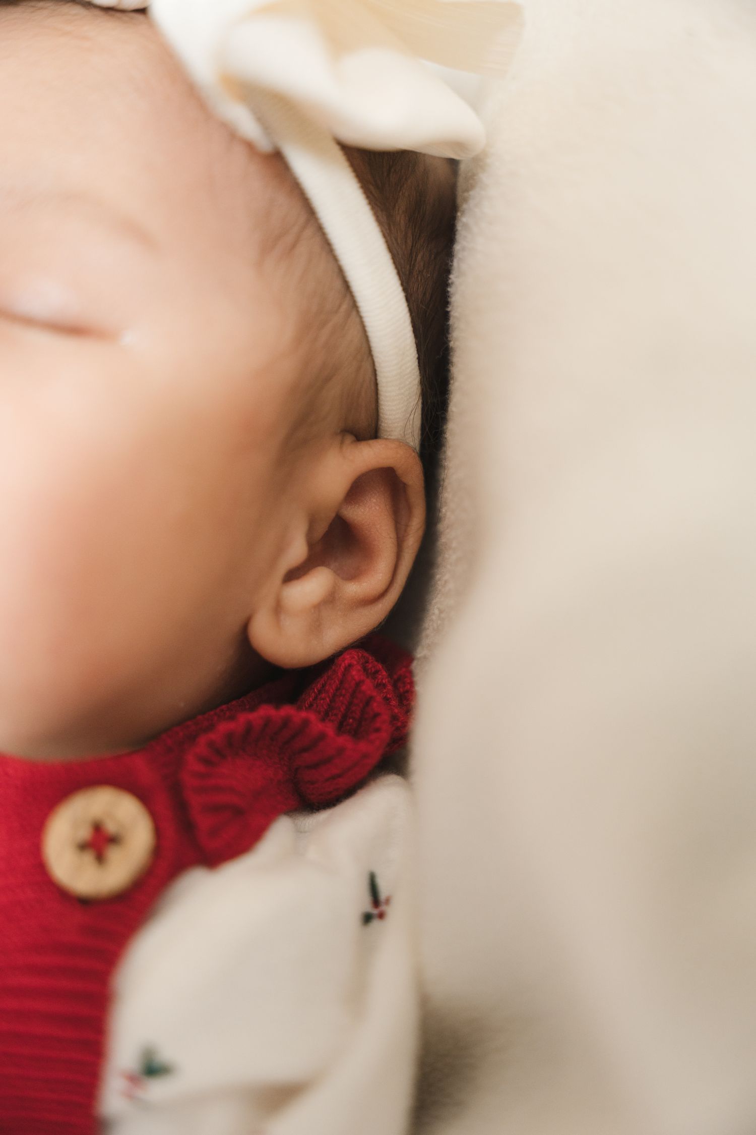 Close-up of a sleeping baby's ear with a white headband and red knit collar.