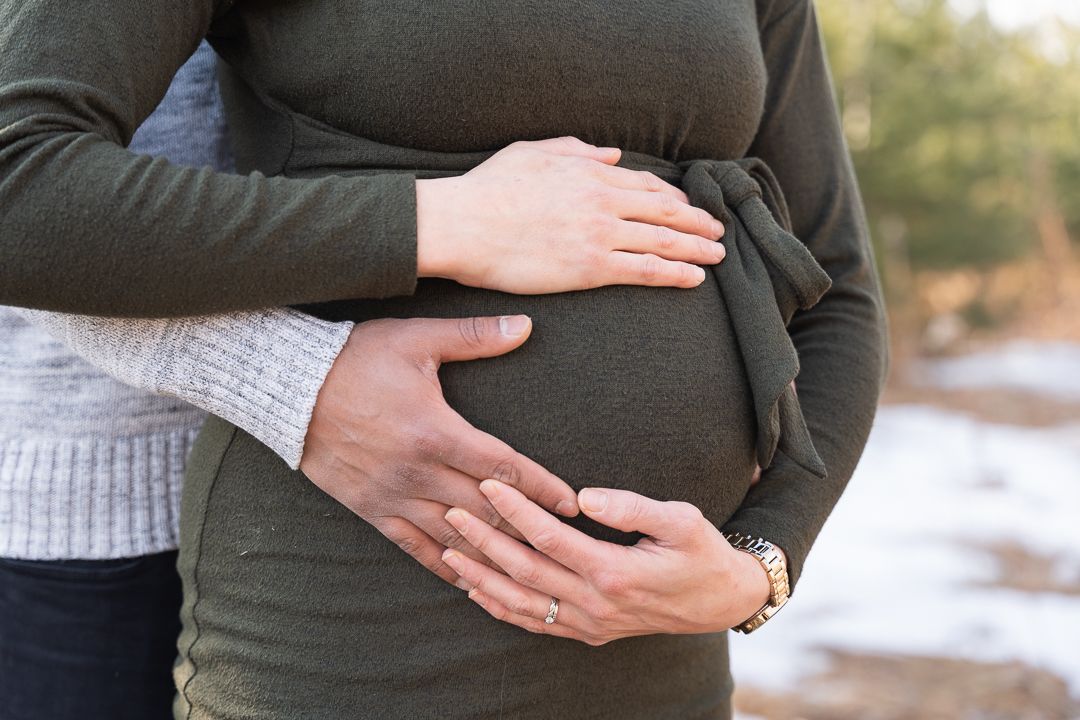 Close-up of hands tenderly cradling a pregnant belly in warm lighting.