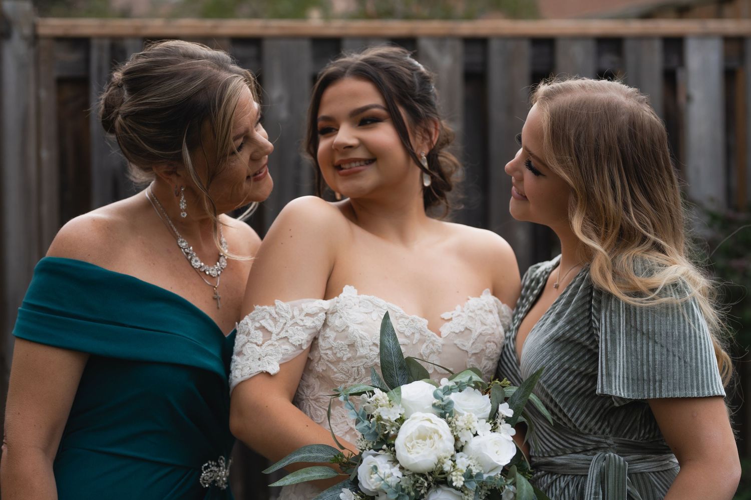 Three bridesmaids in formal dresses share a joyful moment while holding white bouquet.