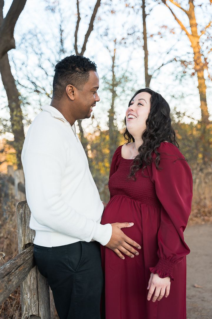 A couple laughs together in an autumn setting with fall foliage in the background.