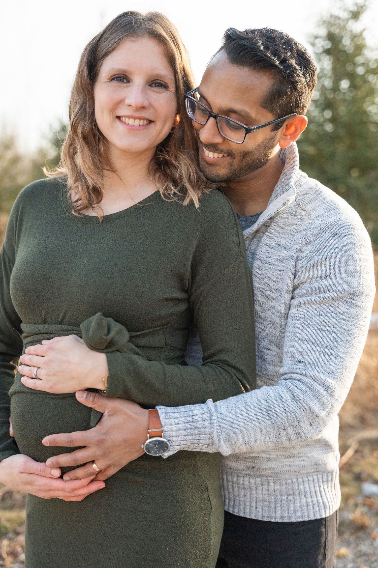 An intimate maternity portrait of a couple in casual sweaters embracing outdoors.