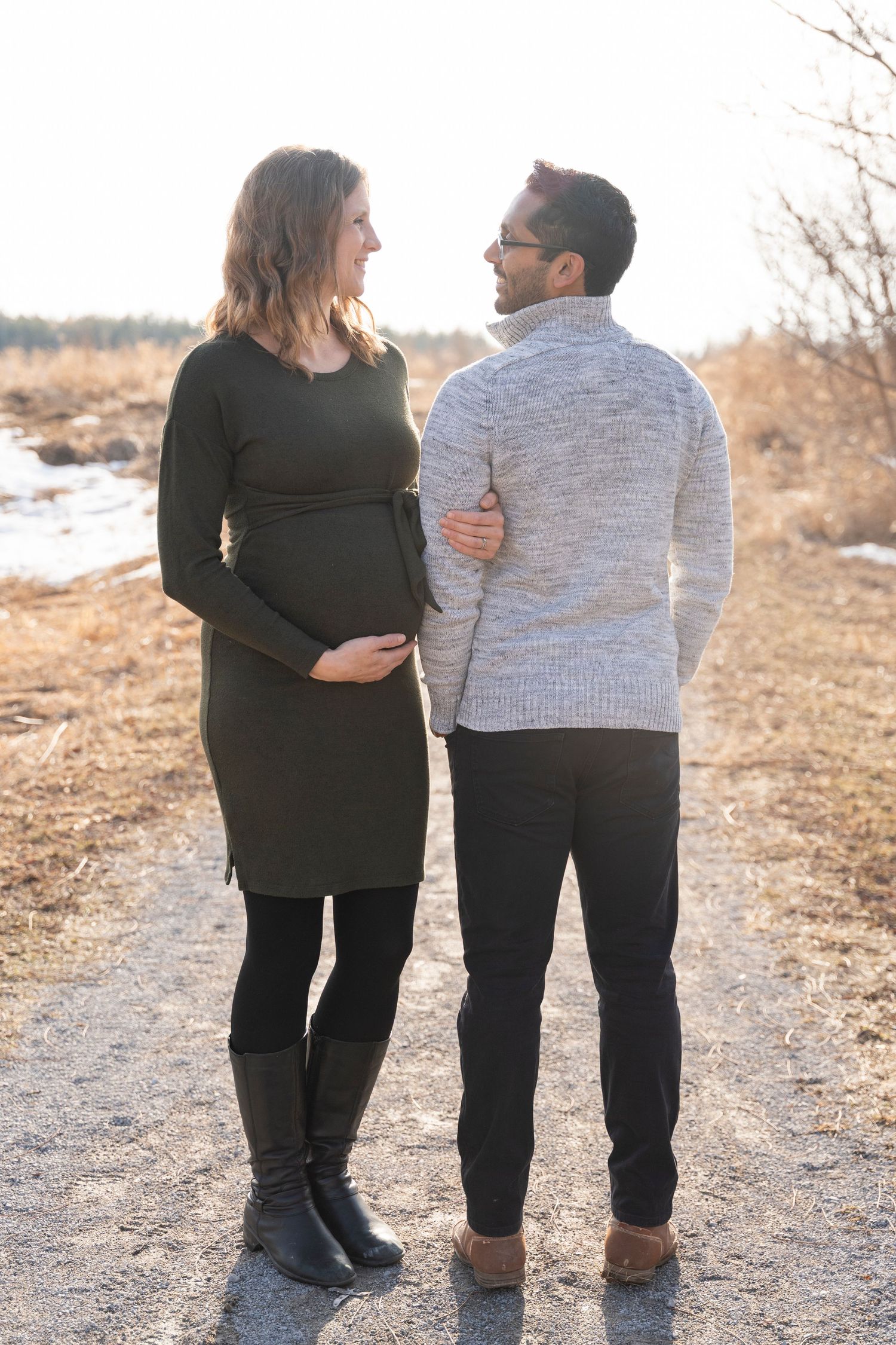 A couple shares an intimate moment during their maternity photoshoot on a nature path.