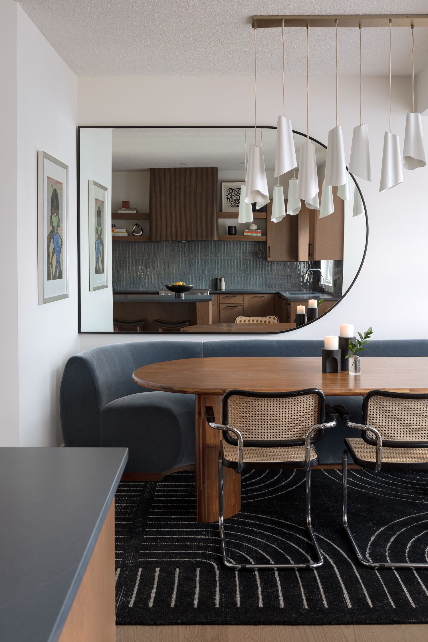Contemporary dining area with blue banquette, cane chairs, round wood table, white pendant lights, and large mirror.