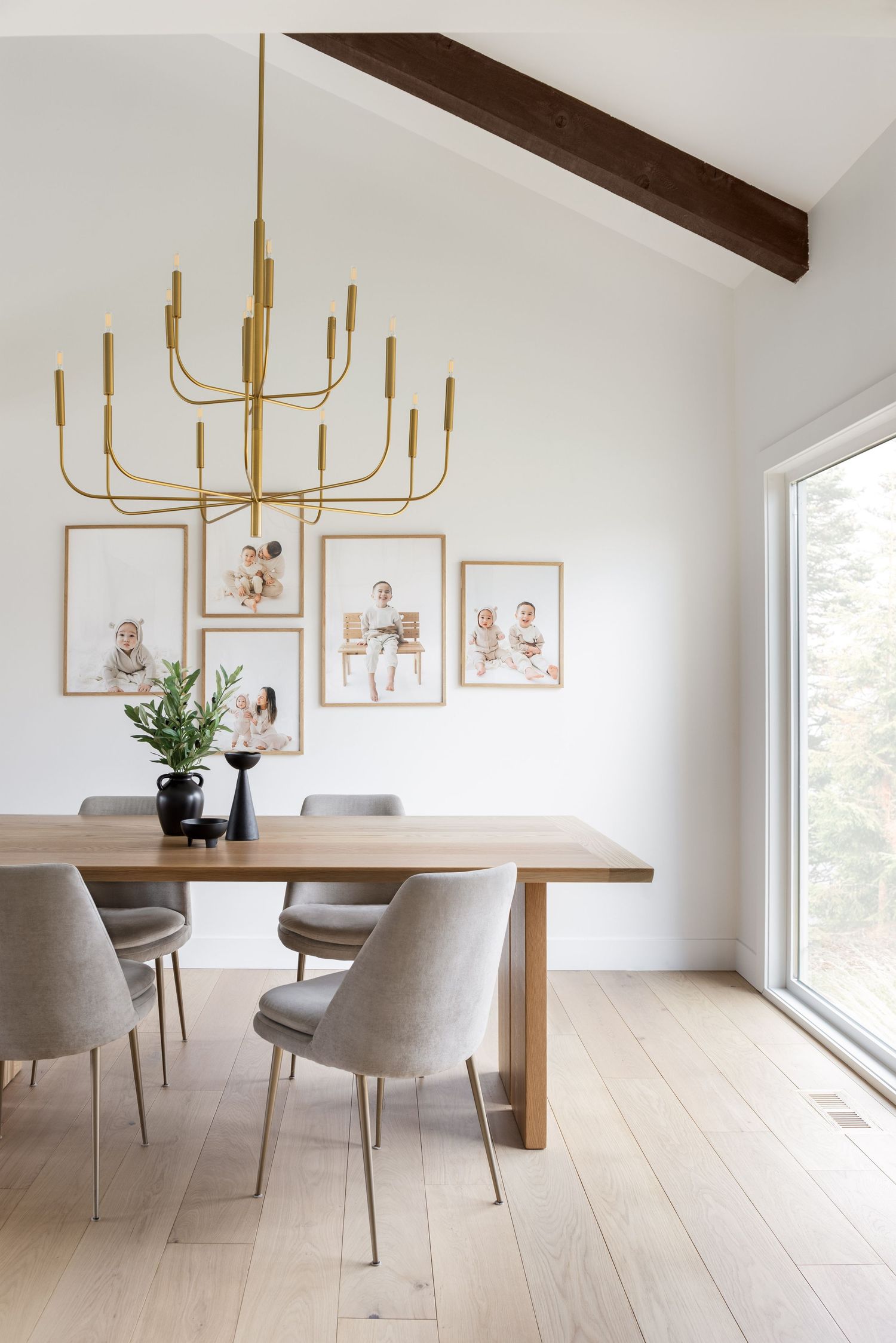 Modern dining room with gold chandelier, wood table, gray chairs, and family photo gallery wall under vaulted ceiling.