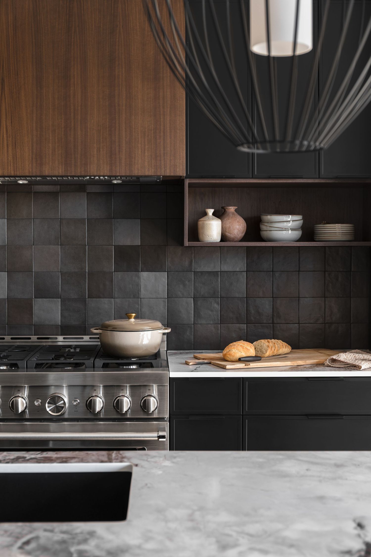 Dramatic dark kitchen with black tile backsplash, walnut cabinets, professional range, and marble countertops.
