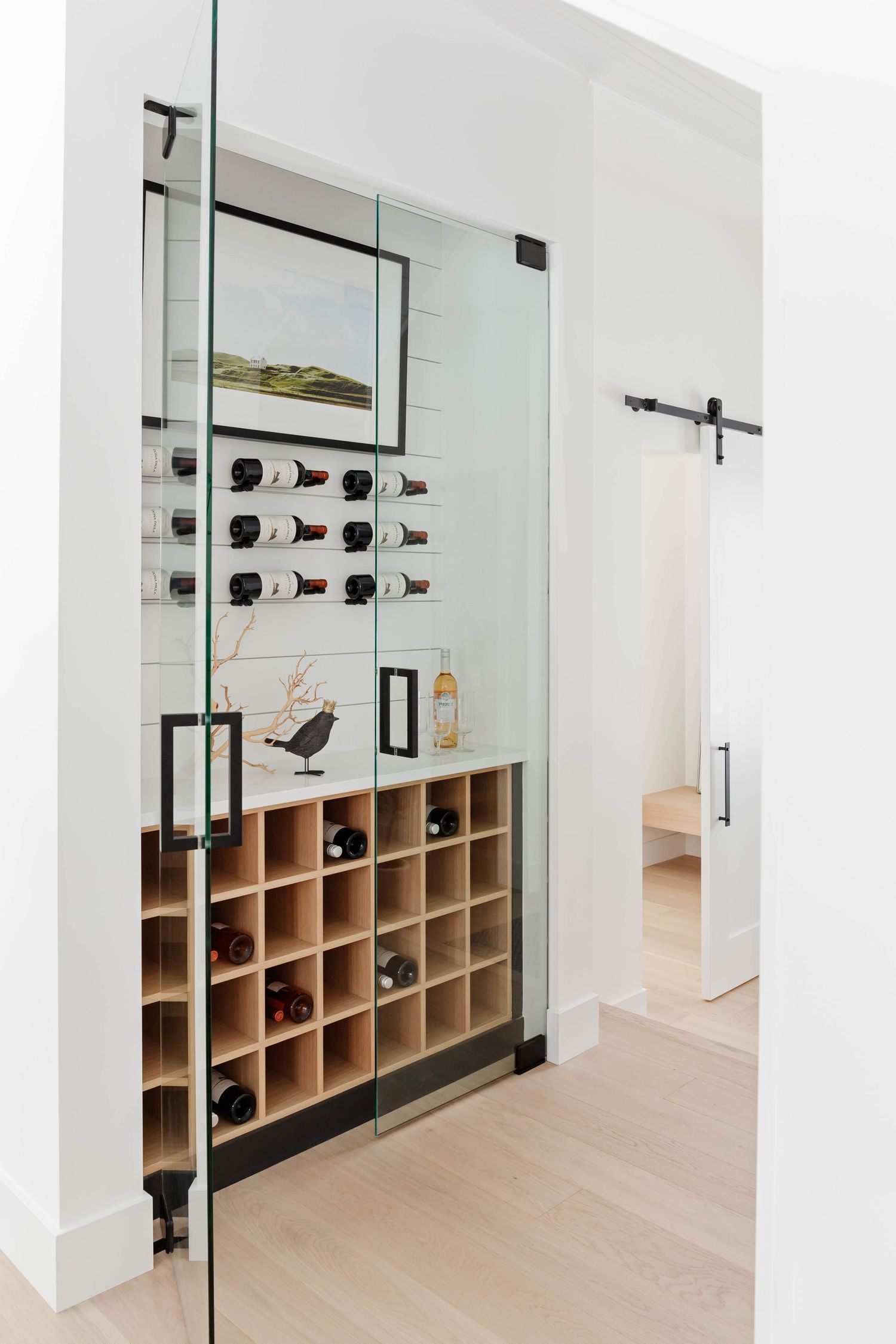 Glass-enclosed wine cellar with wall-mounted racks and wooden cube wine storage unit.