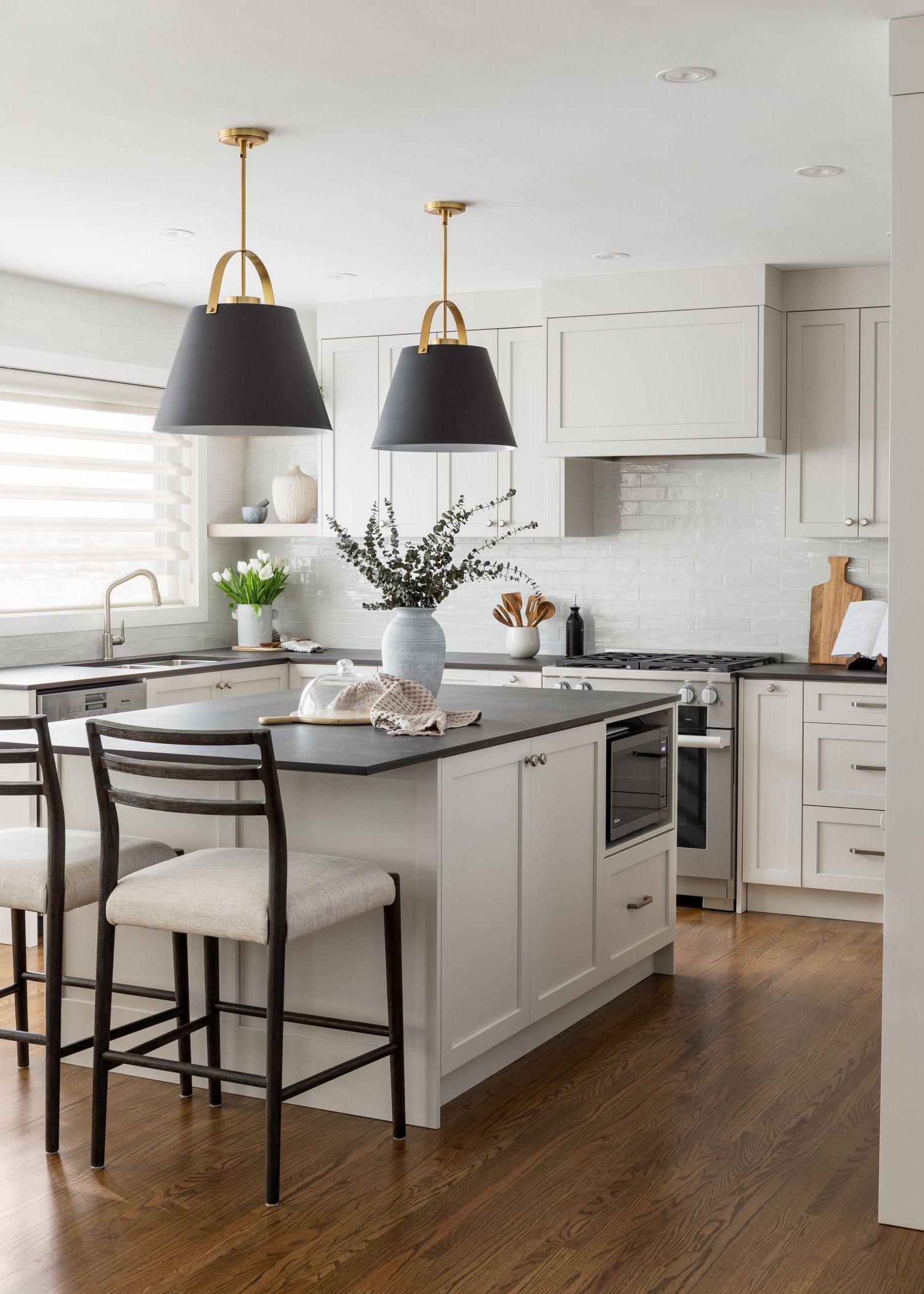 White kitchen with black island countertop, pendant lights, and bar stools on hardwood floors.
