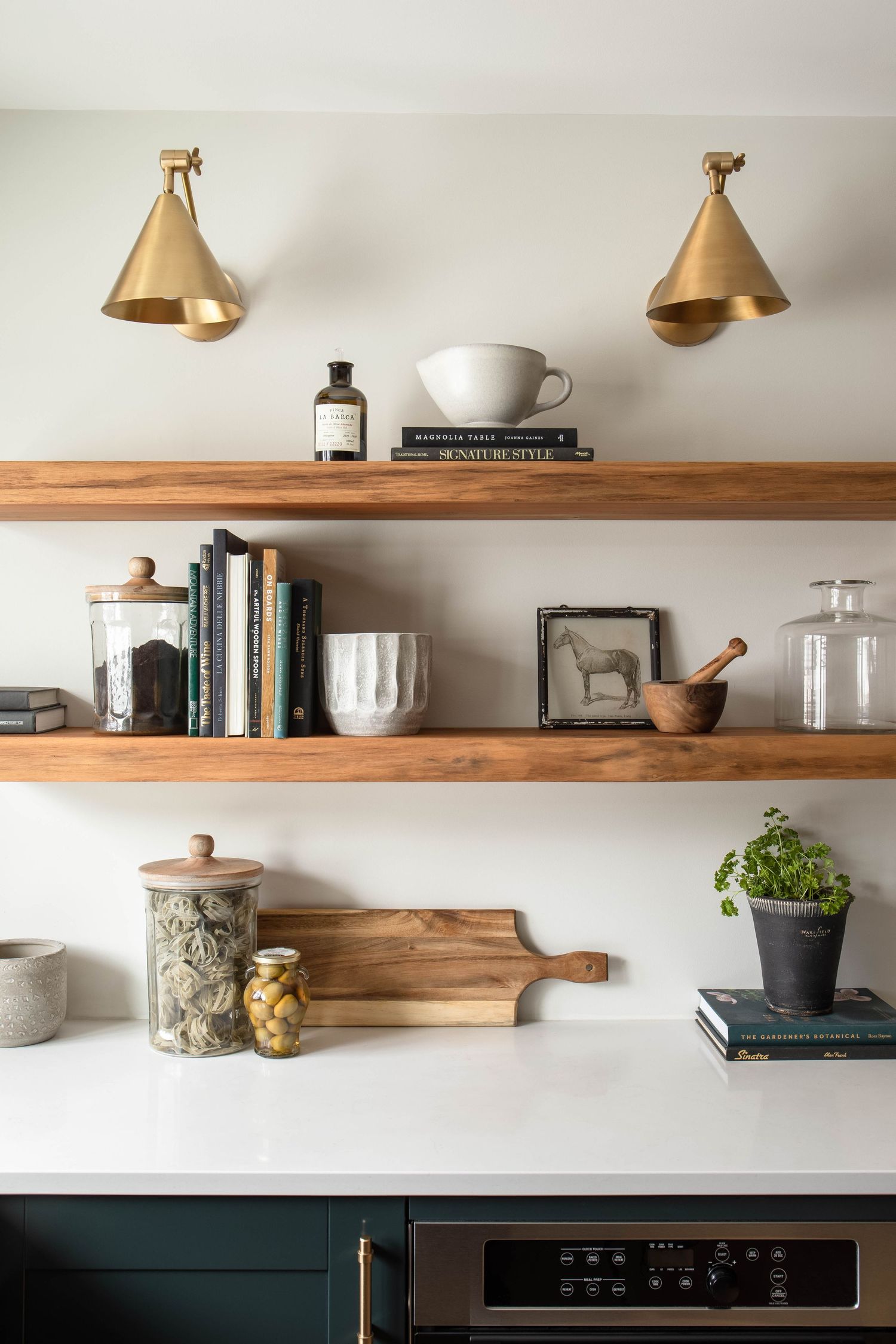Styled kitchen open shelves with walnut wood, brass cone sconces, books, ceramics, and decorative kitchen accessories.