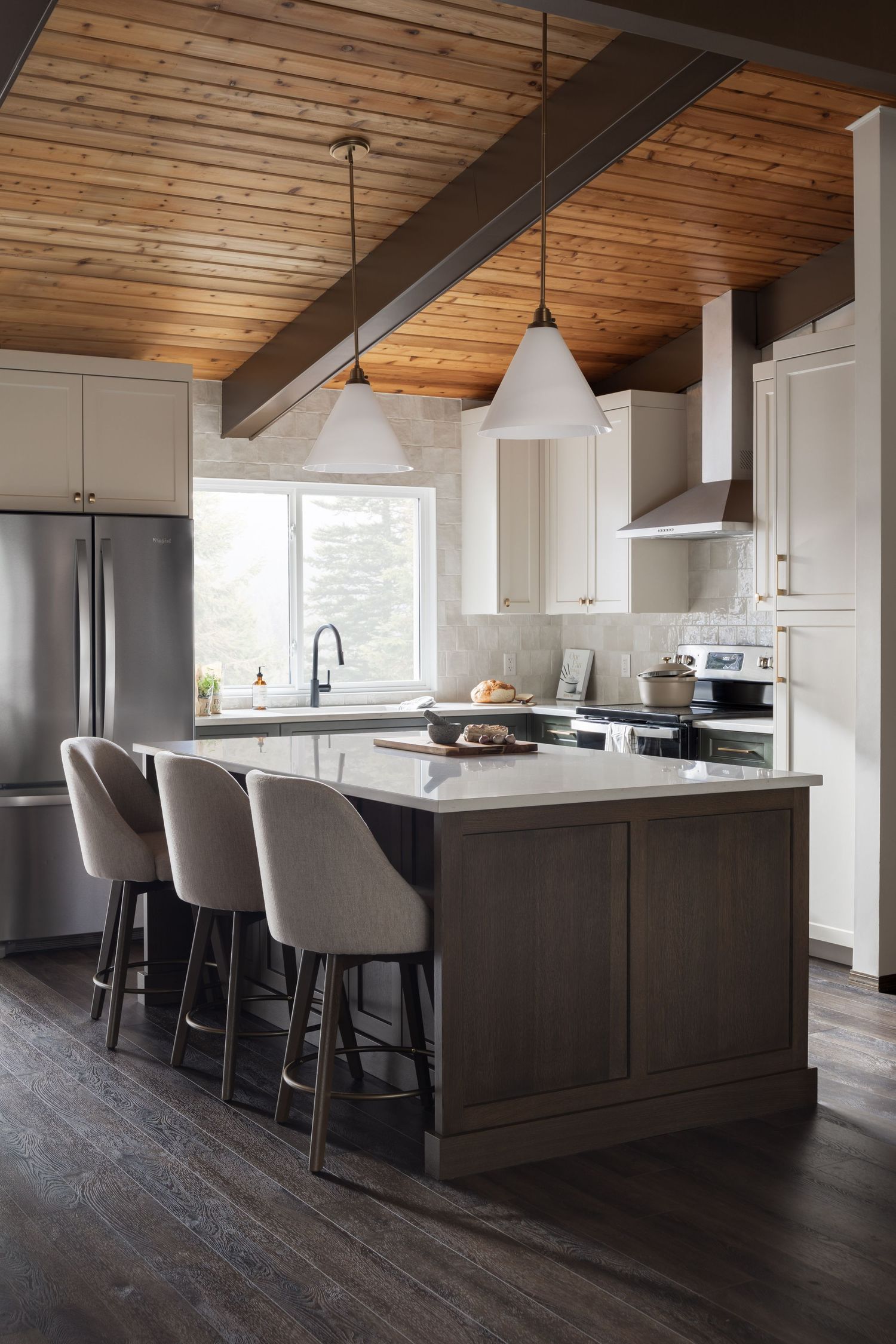 Modern kitchen with wood ceiling, dark island, white cabinets, pendant lights, and upholstered bar stools.
