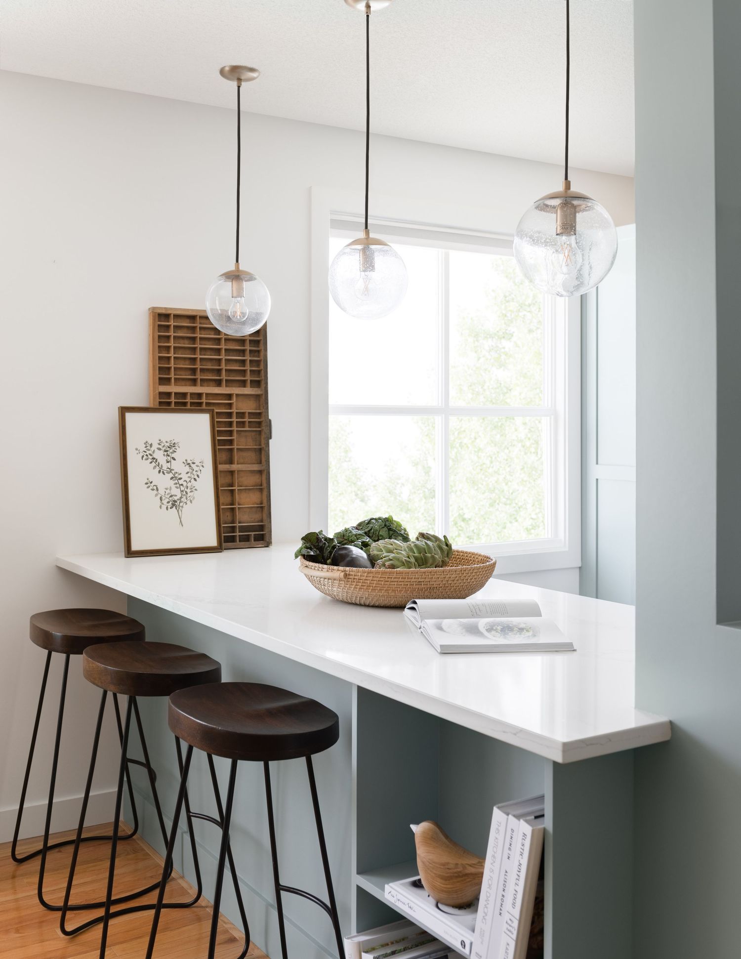 Breakfast bar with white countertop, teal base, dark stools, and globe pendant lights.