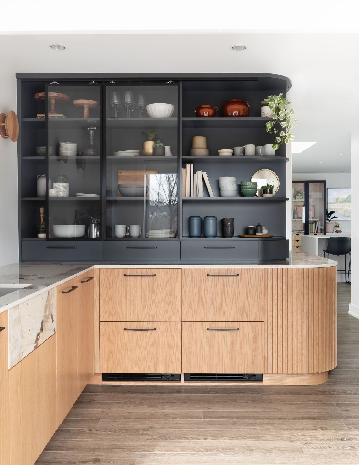 Contemporary kitchen with fluted light wood island, navy blue open shelving displaying ceramics, and glass-front upper cabinets.