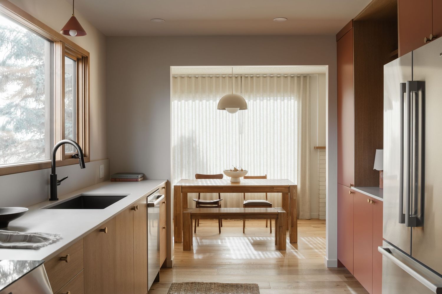 Modern kitchen with light wood cabinets, white countertops, and dining area with pendant lighting by Interior photographer Rebecca Frick
