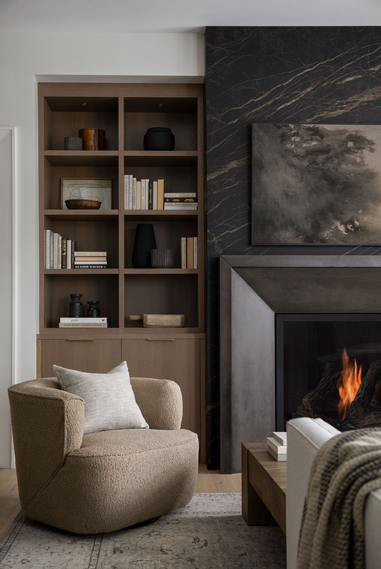 Warm living room with lit fireplace, dark marble surround, oak built-ins, and curved boucle armchair.